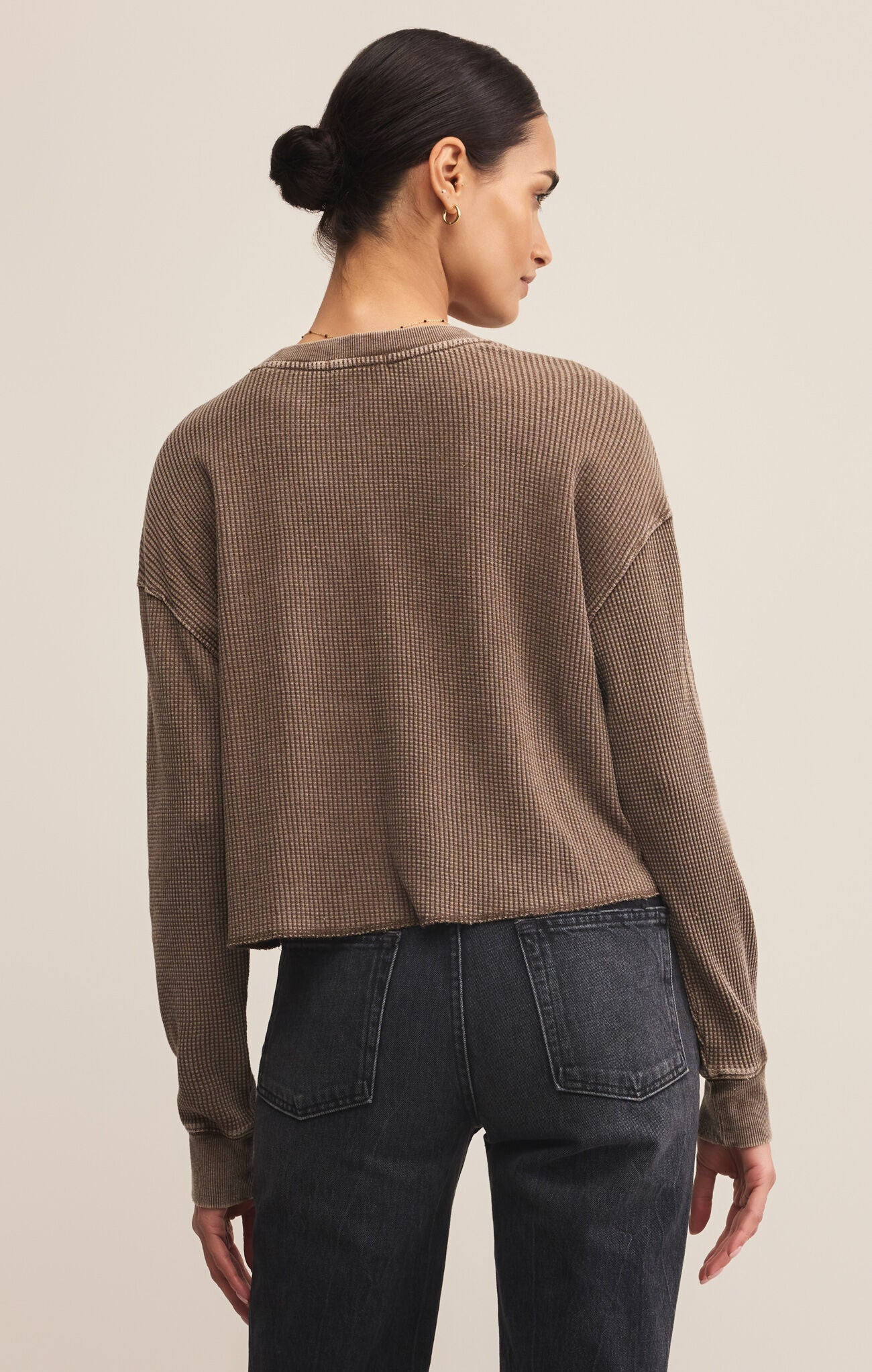 Woman wearing a brown textured sweater and dark jeans on a beige background