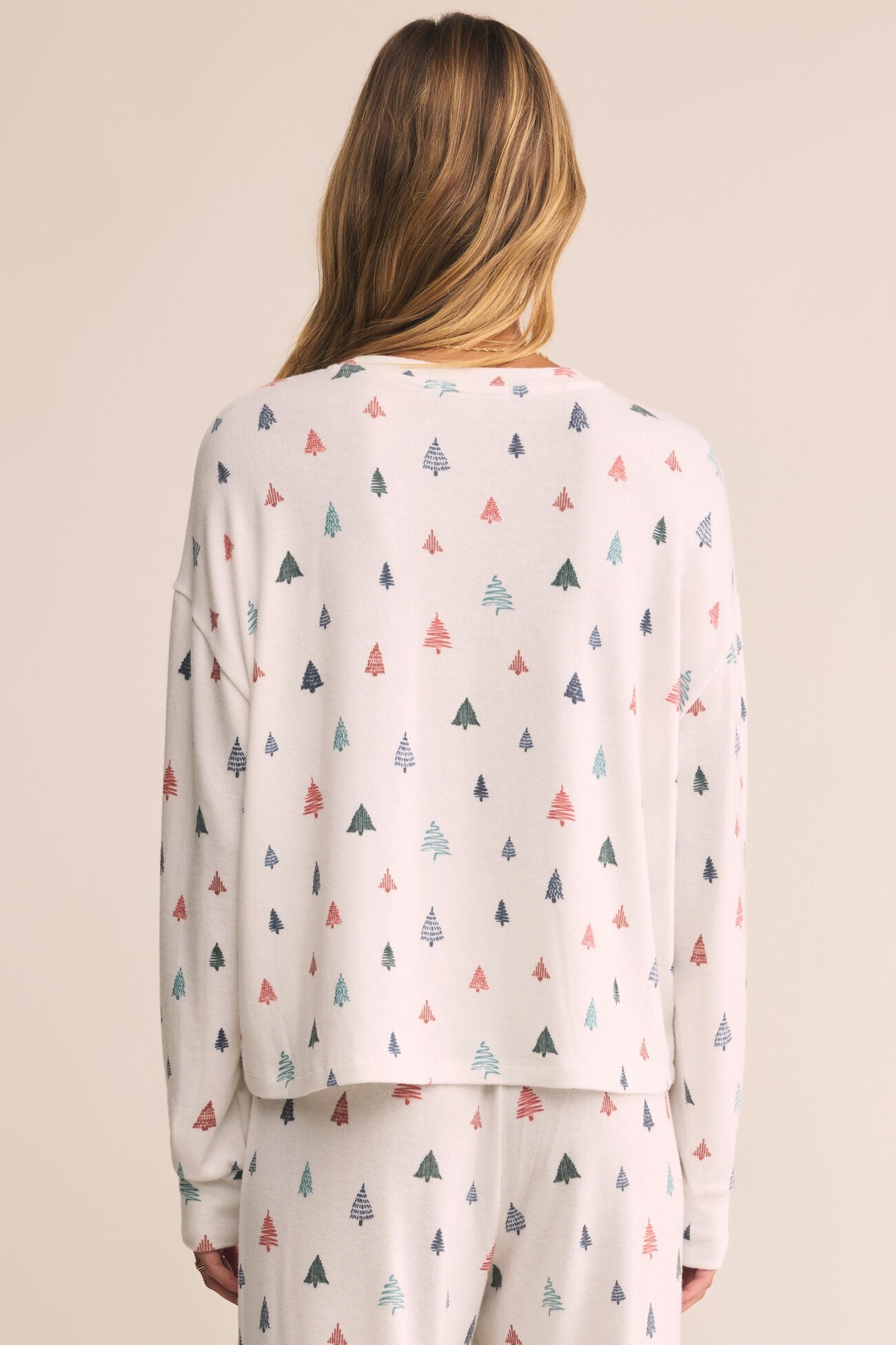 Person wearing a white long-sleeve shirt with colorful tree pattern on a beige background