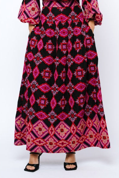 Person wearing a long, patterned dress with pink and red geometric design on a white background