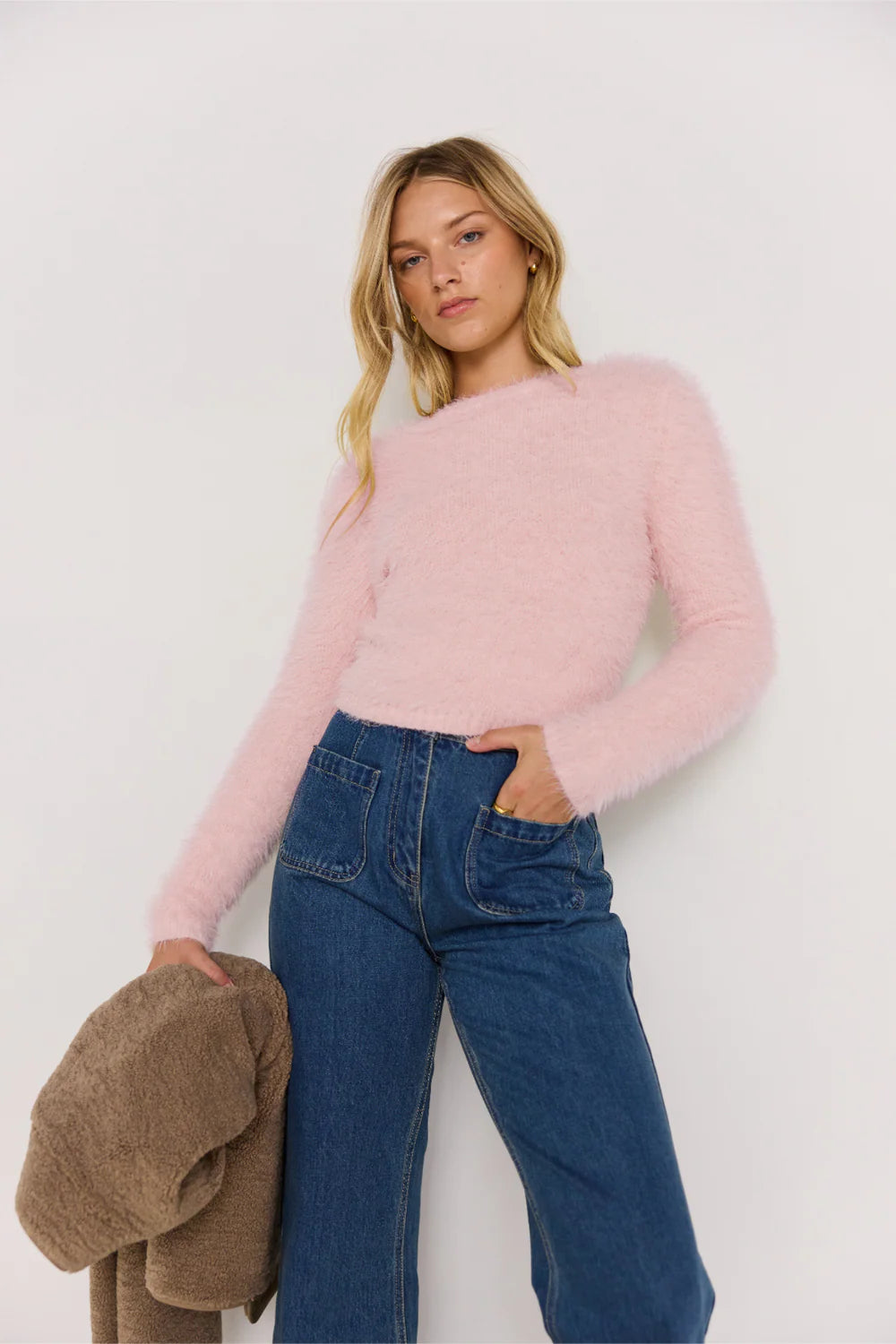 Woman wearing a pink sweater and blue jeans against a white background