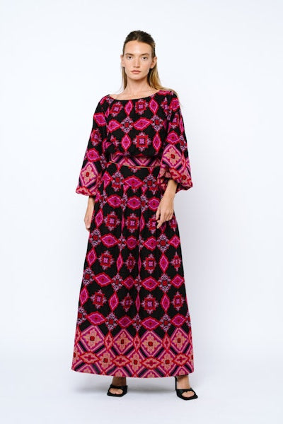 Woman wearing a long, patterned dress with pink and black design on a white background