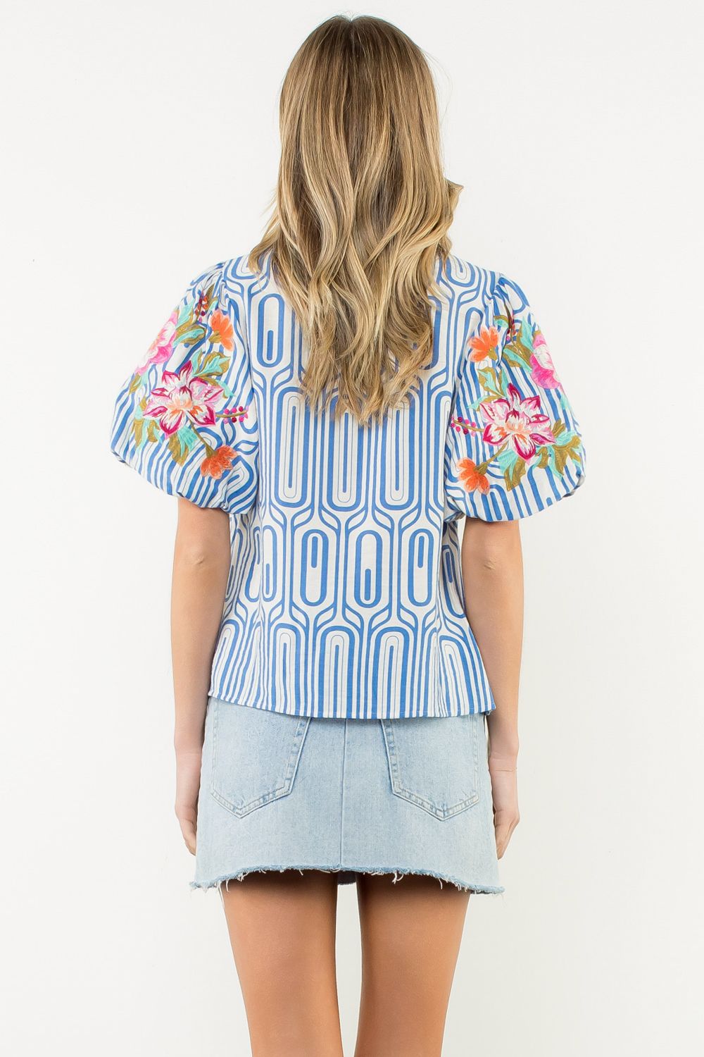 Woman wearing a blue patterned top with floral sleeves on a white background