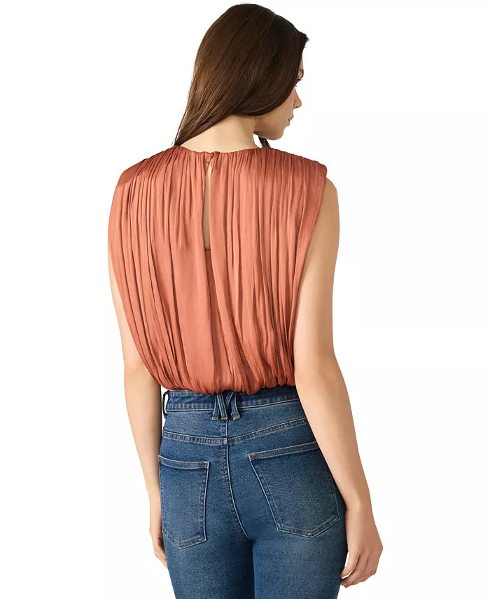 Woman wearing a rust-colored sleeveless top and blue jeans on a white background