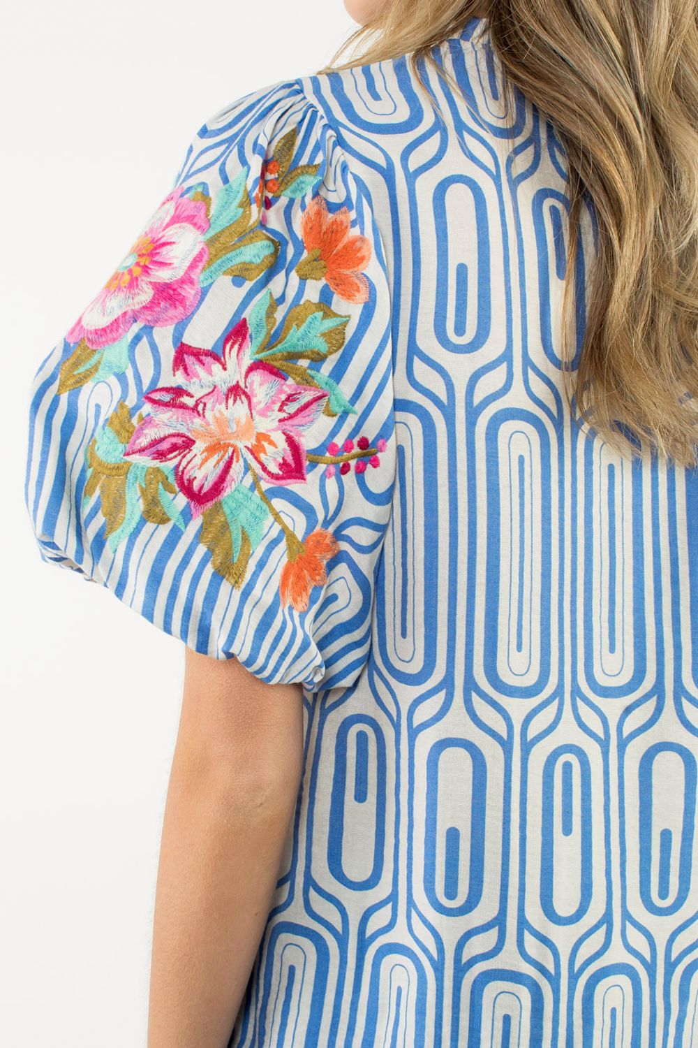 Blue geometric patterned shirt with colorful floral embroidery on a white background