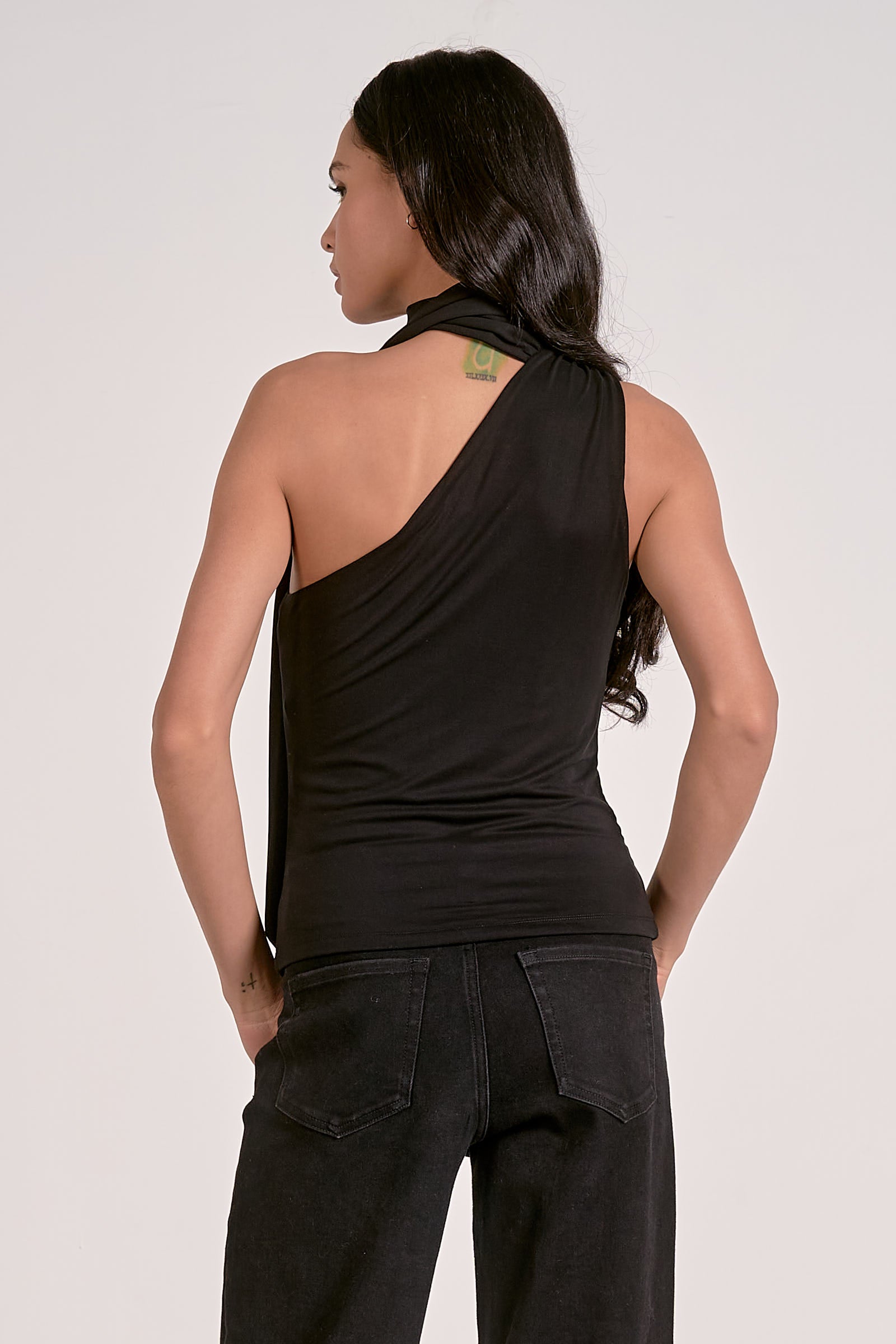 Woman wearing a black one-shoulder top and dark pants on a light background