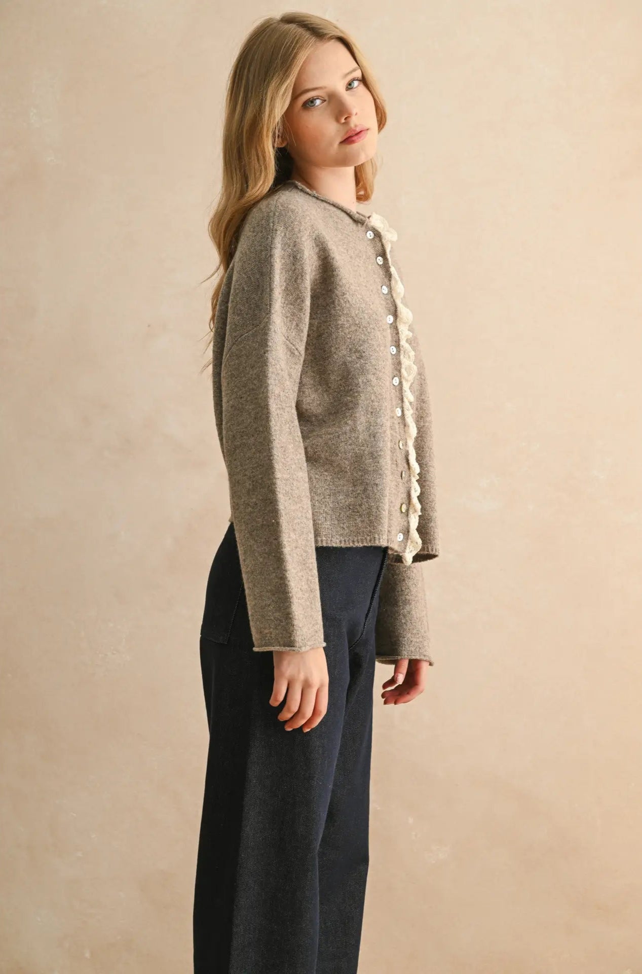 Woman wearing a beige cardigan with ruffled details on a beige background