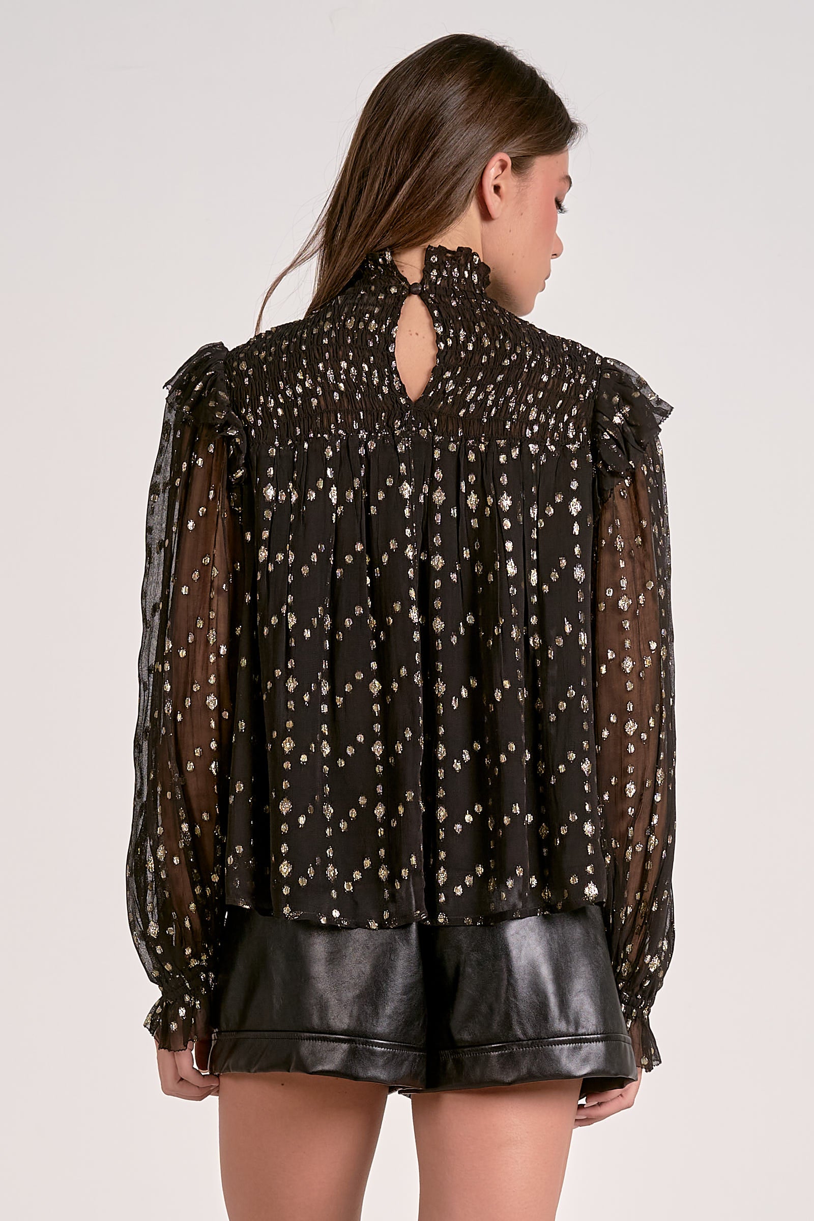 Woman wearing a black blouse with sheer sleeves and a cut-out back design on a white background