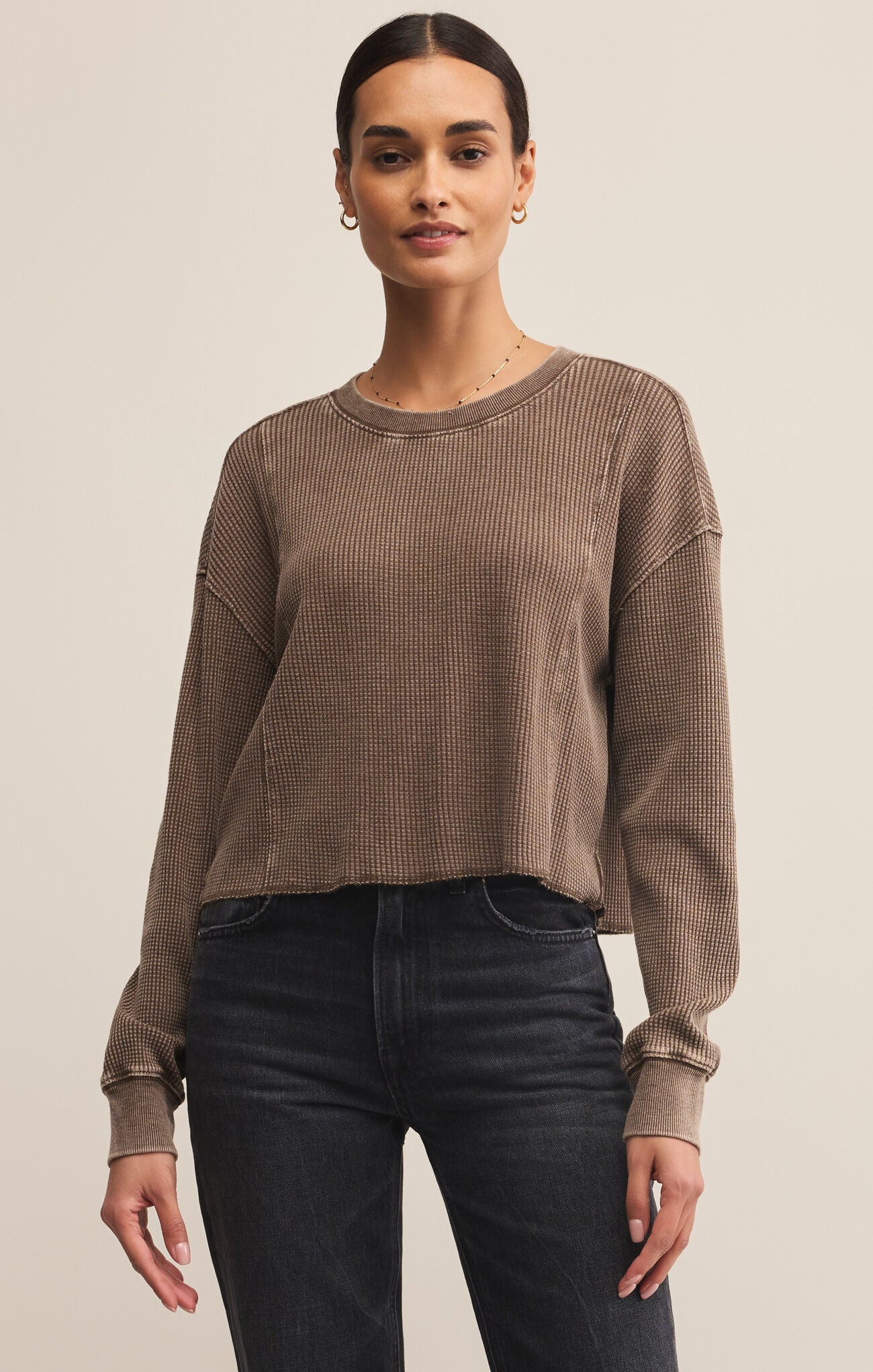 Woman wearing a brown ribbed sweater and black pants on a beige background