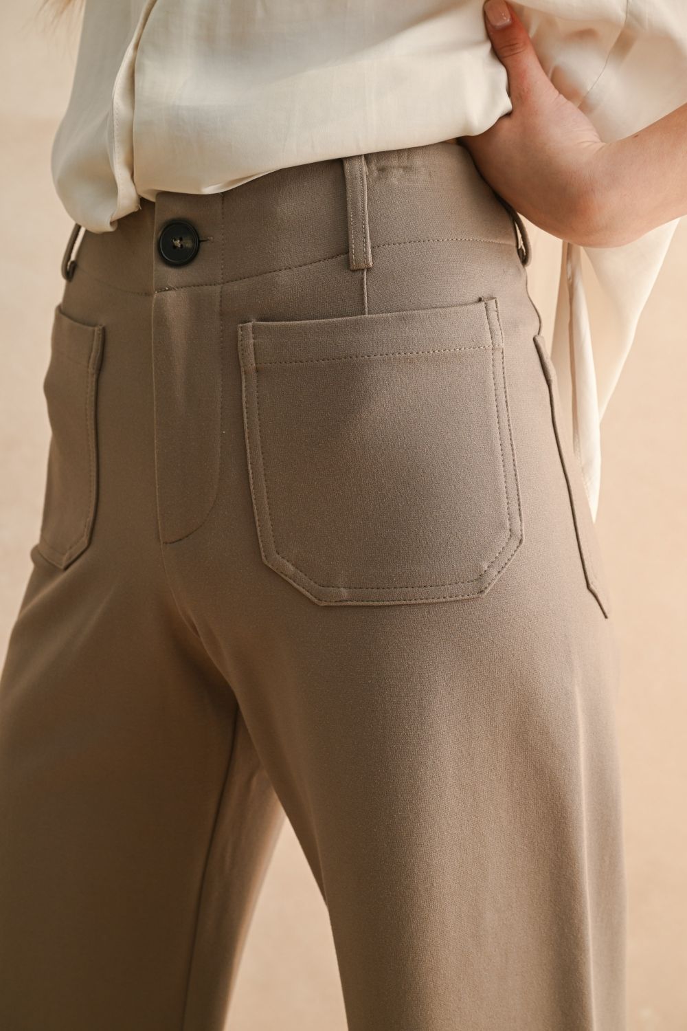Beige pants with a button and pocket detail on a neutral background