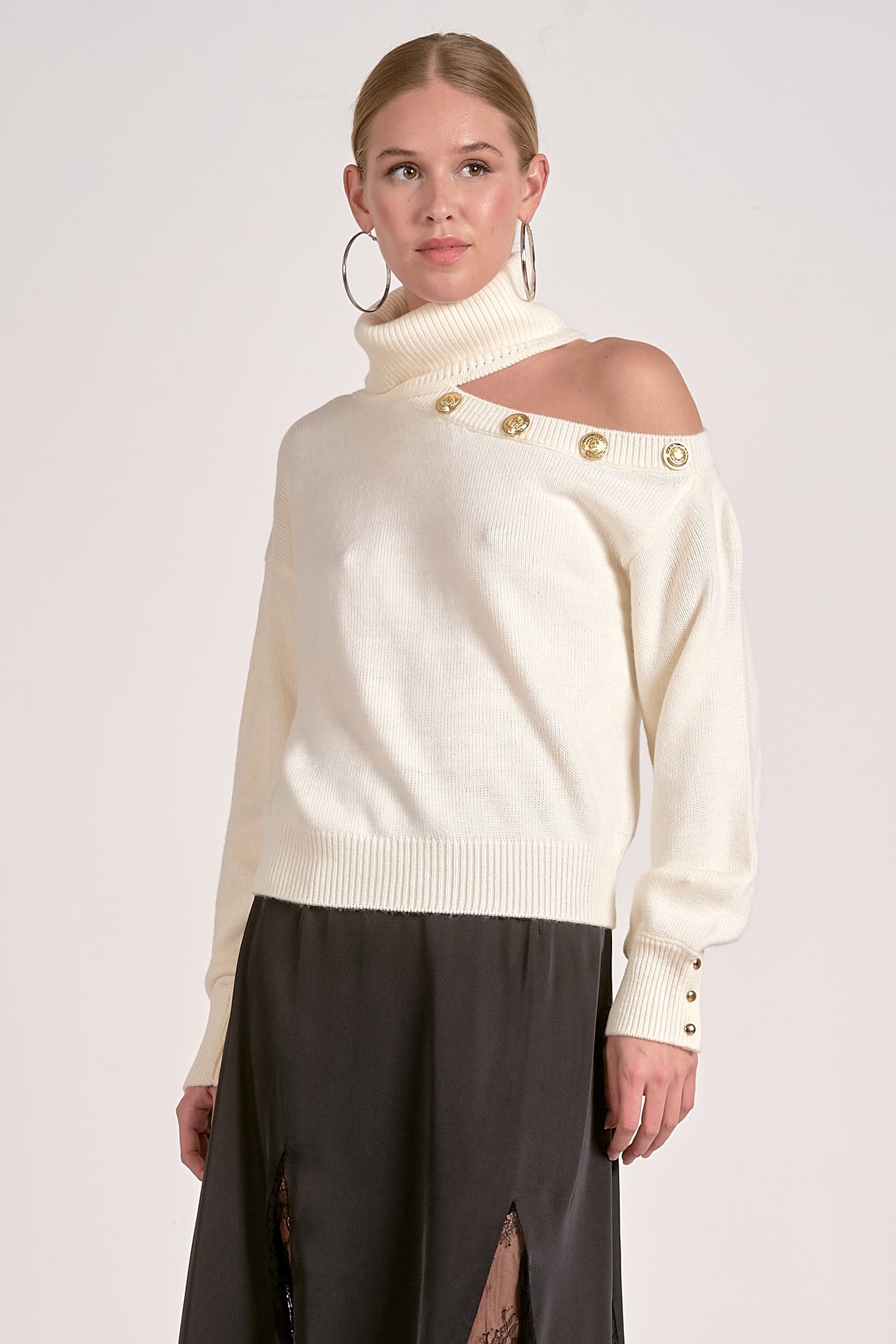 Woman wearing a cream sweater with gold buttons on a white background