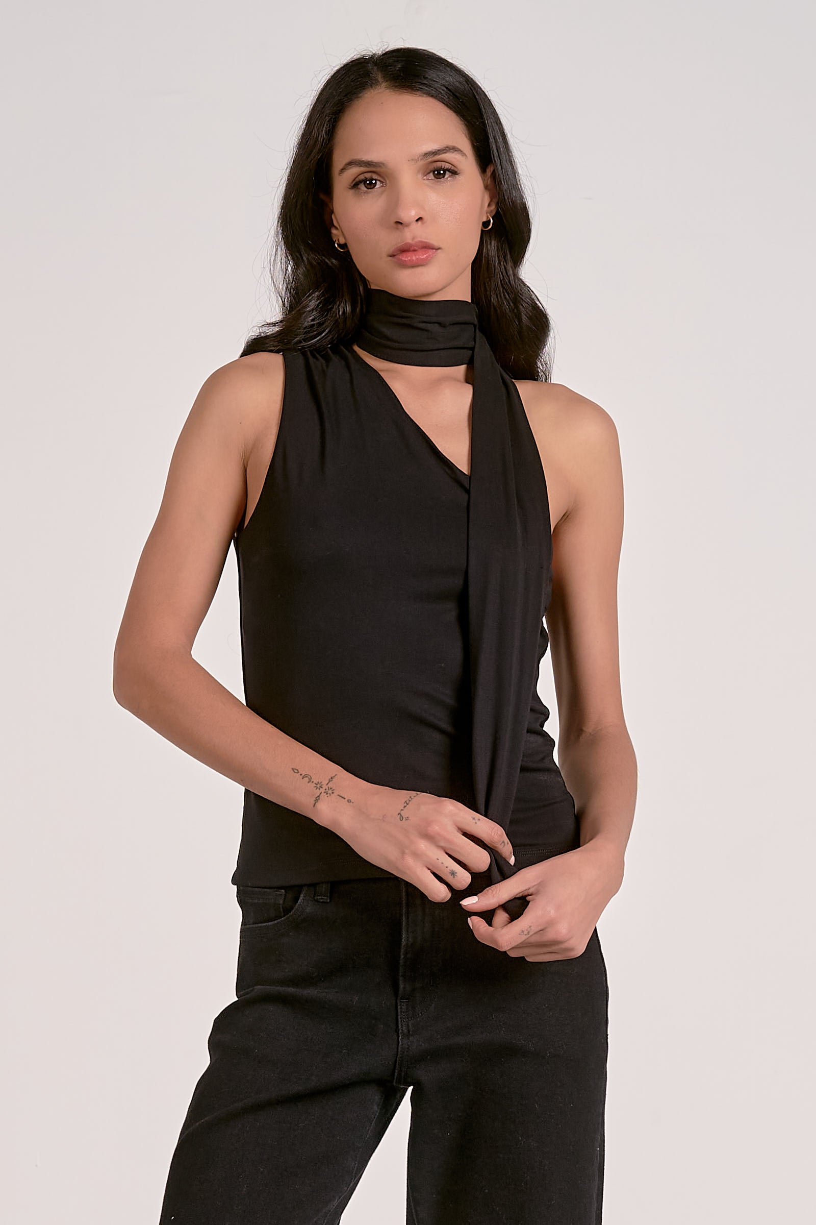Woman wearing a black sleeveless top and pants with a black scarf on a white background