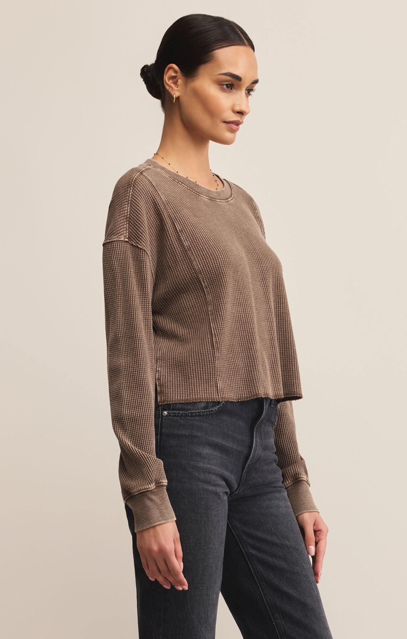 Woman wearing a brown ribbed sweater and dark jeans against a beige background