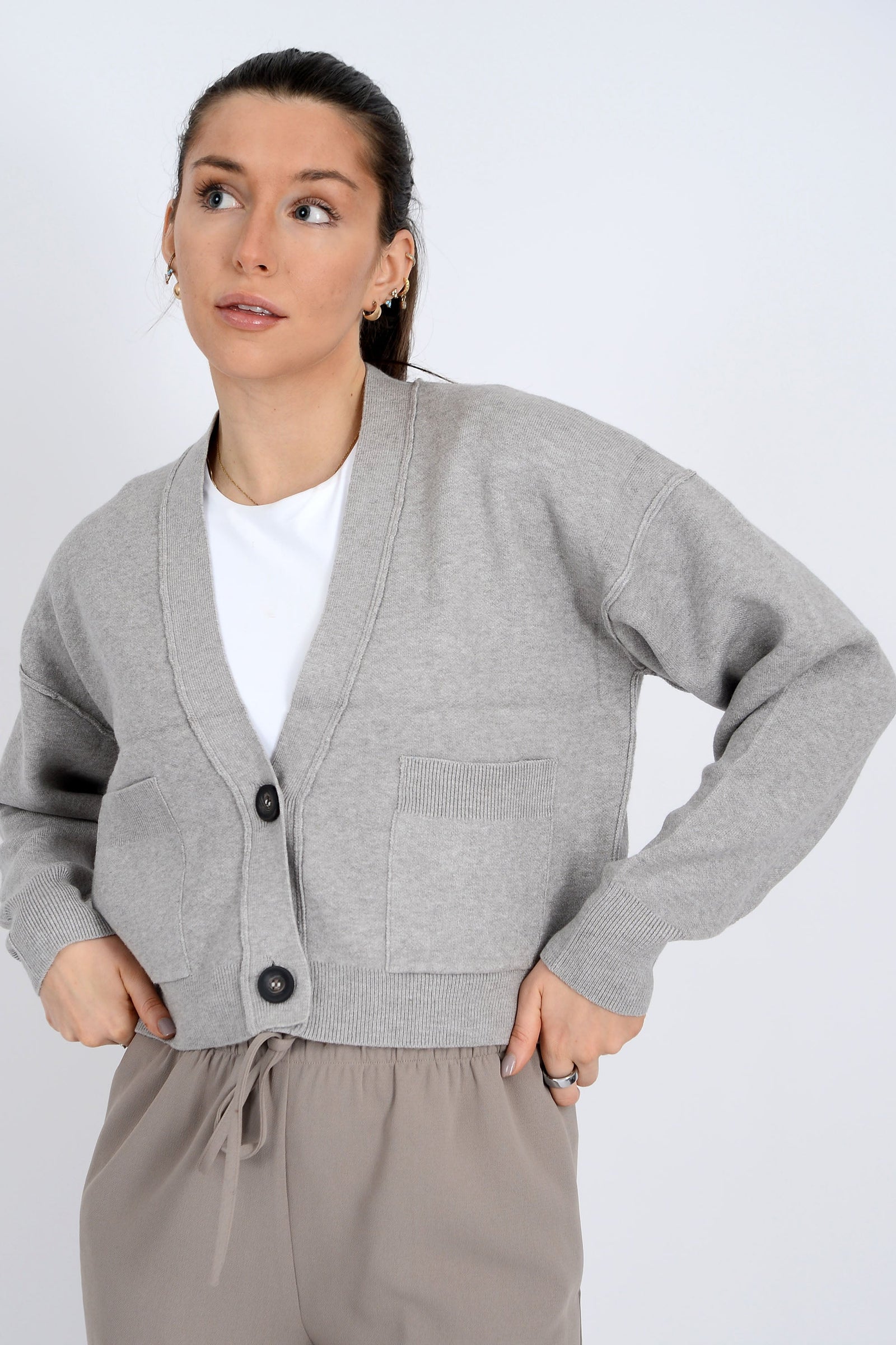 Woman wearing a gray cardigan over a white shirt with beige pants on a white background