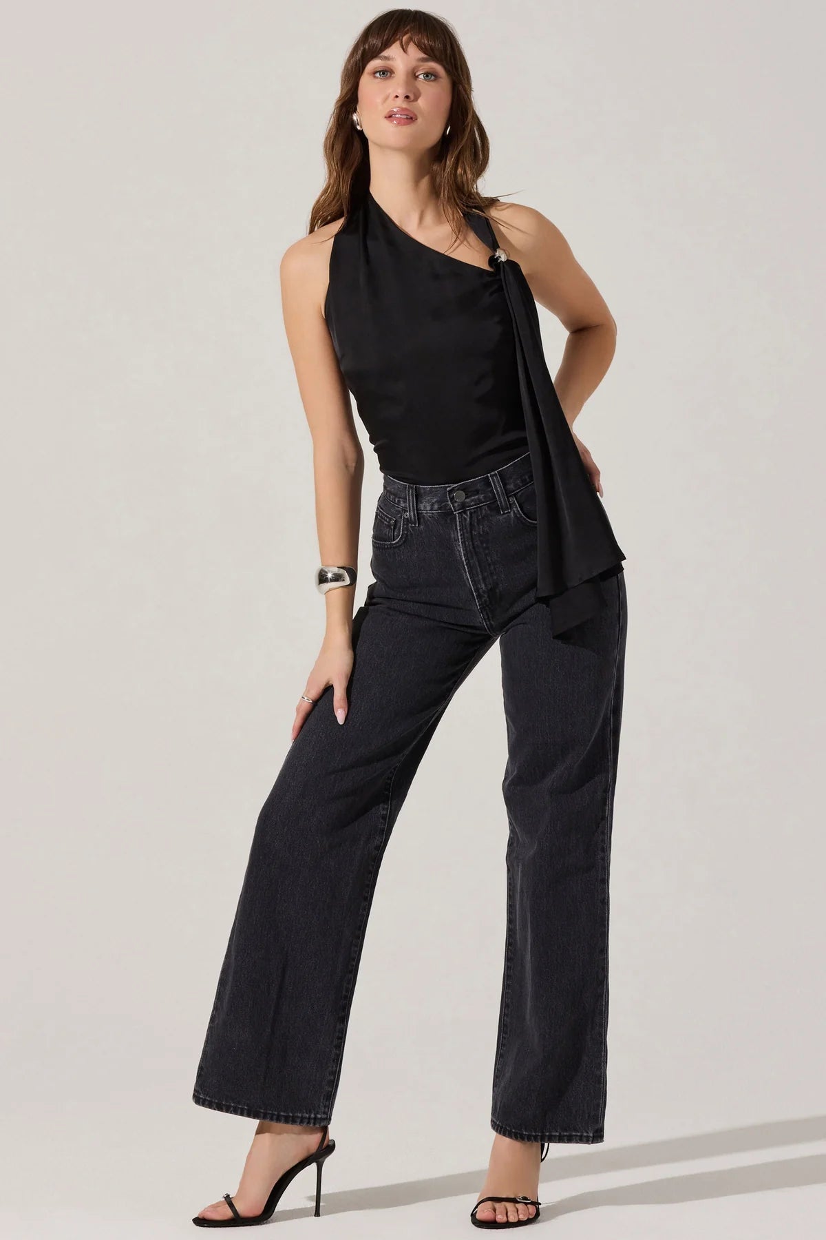 Woman wearing a black sleeveless top and dark jeans on a light gray background