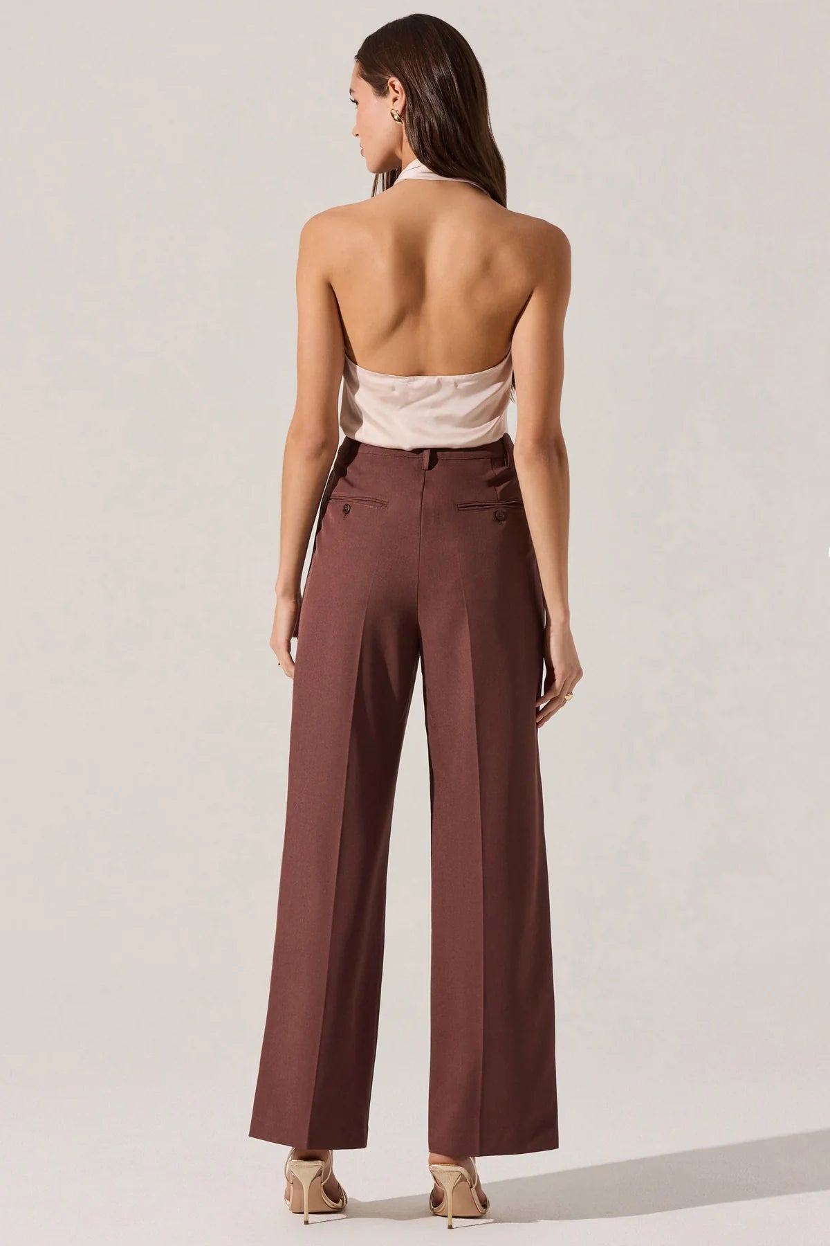 Woman wearing a white top and brown high-waisted pants on a plain background