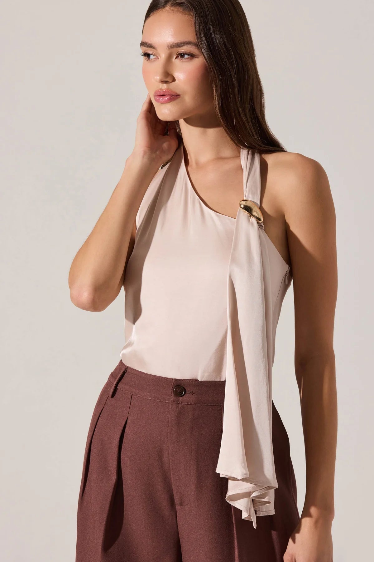 Woman wearing a beige halter top and brown pants against a plain background