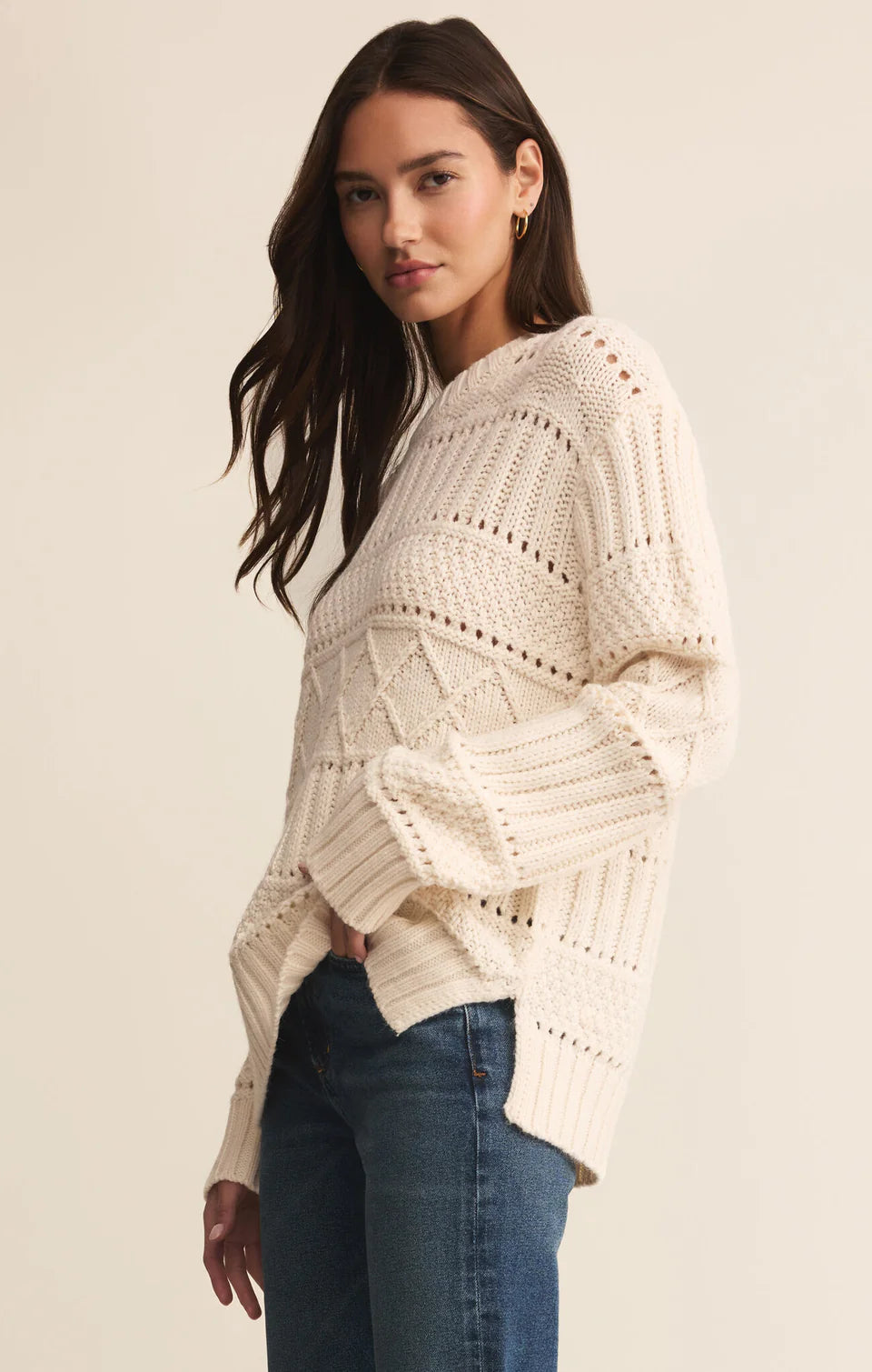 Woman wearing a cream-colored knitted sweater and blue jeans on a beige background