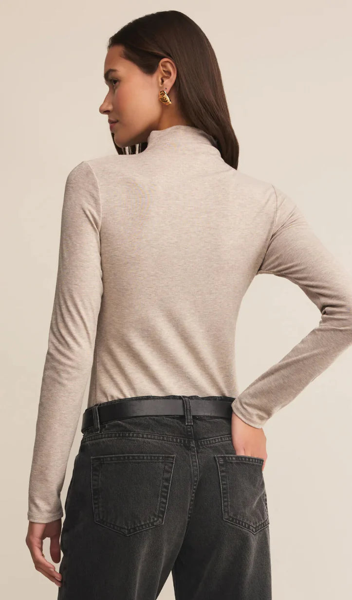 Woman wearing a beige long-sleeve top and dark jeans on a beige background