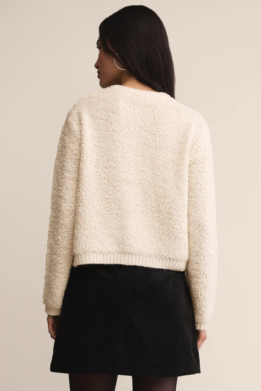 Person wearing a beige knitted sweater and black skirt on a plain background