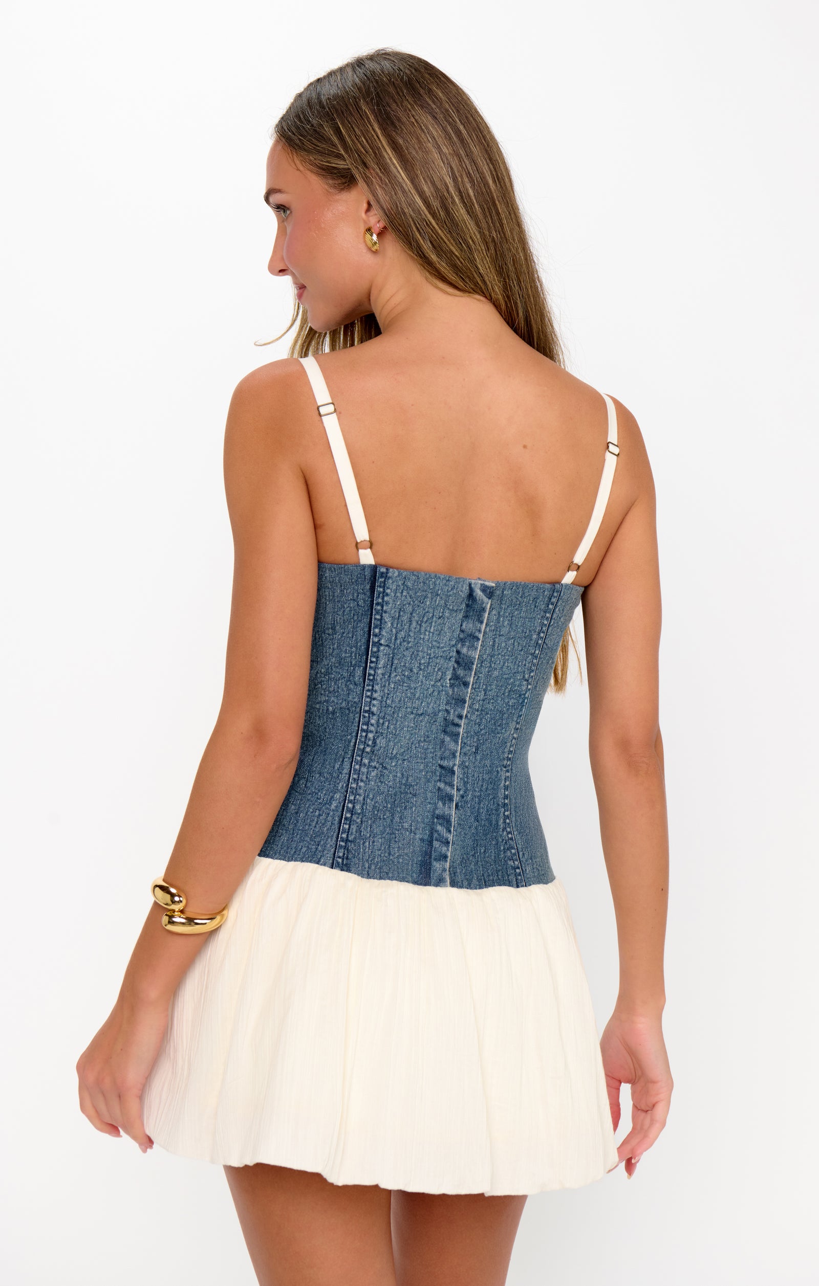 Woman wearing a denim and white dress with thin straps on a white background
