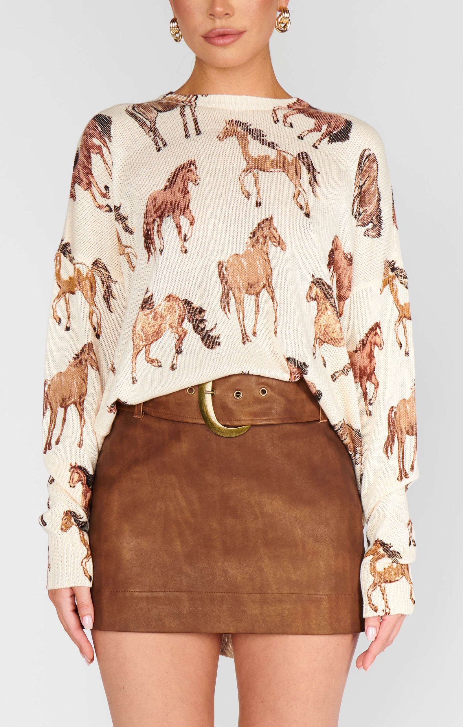 Woman wearing a sweater with horse pattern and brown leather skirt on a plain background