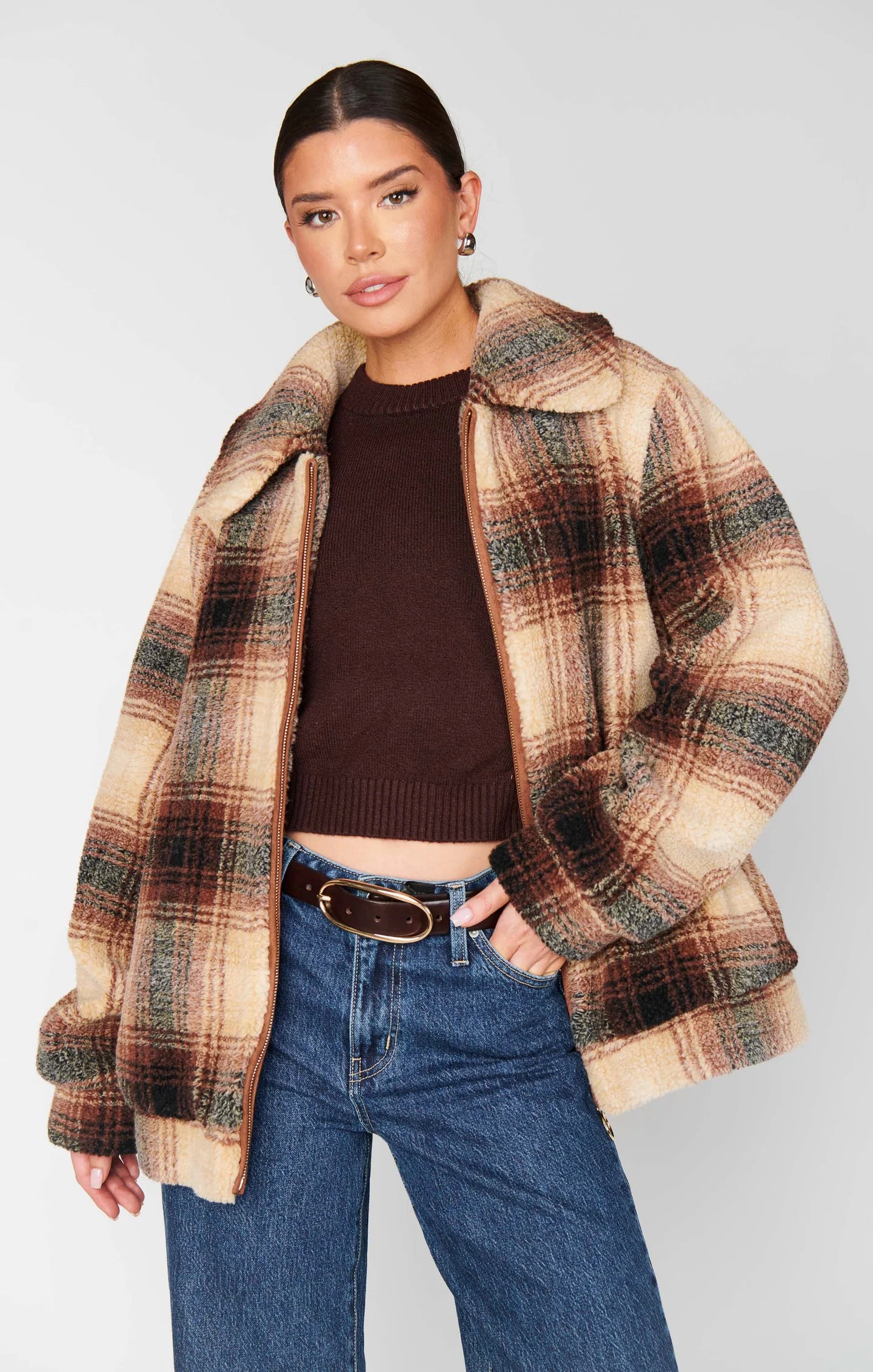 Woman wearing a plaid jacket over a brown sweater and blue jeans on a white background