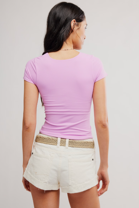 Woman wearing a pink top and white shorts with a beige belt on a plain background