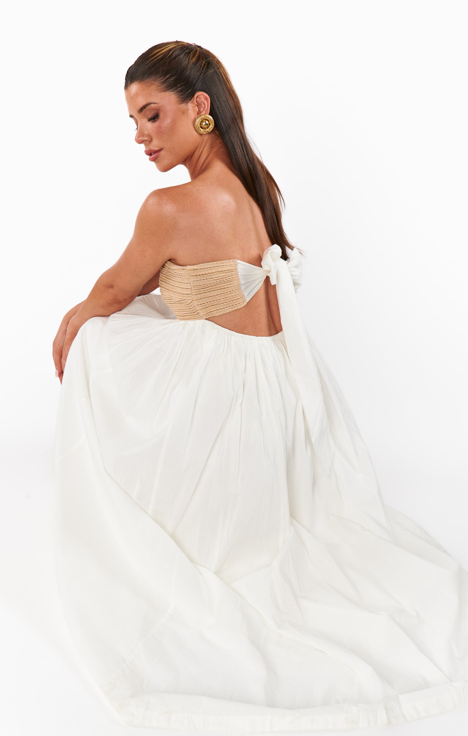 Woman in a white dress with a beige strapless top on a plain background
