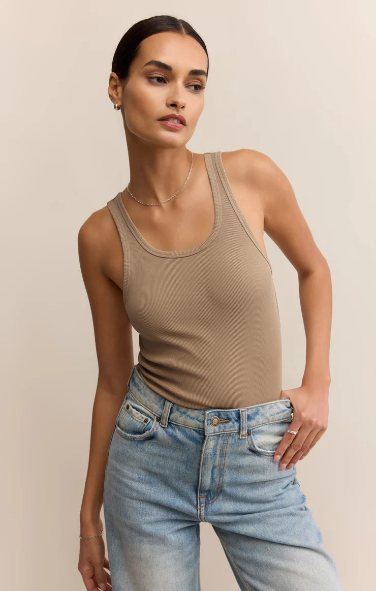 Woman wearing a beige tank top and blue jeans against a beige background
