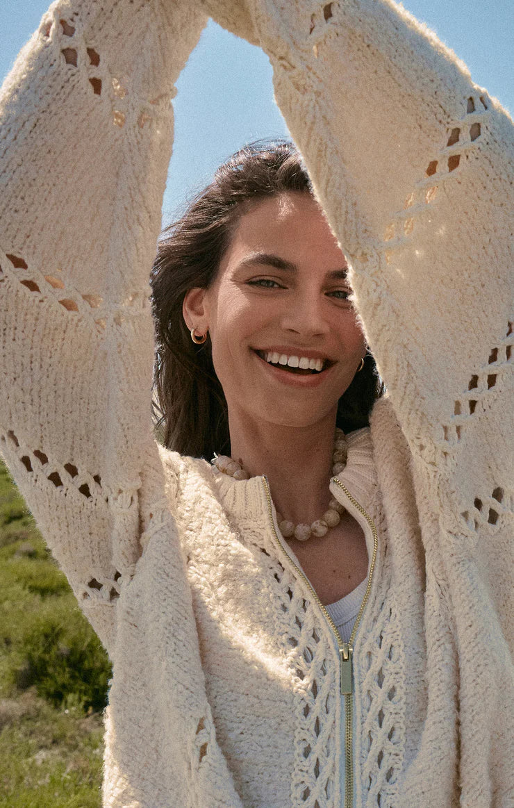 Woman wearing a cream-colored crochet cardigan with a blurred natural background