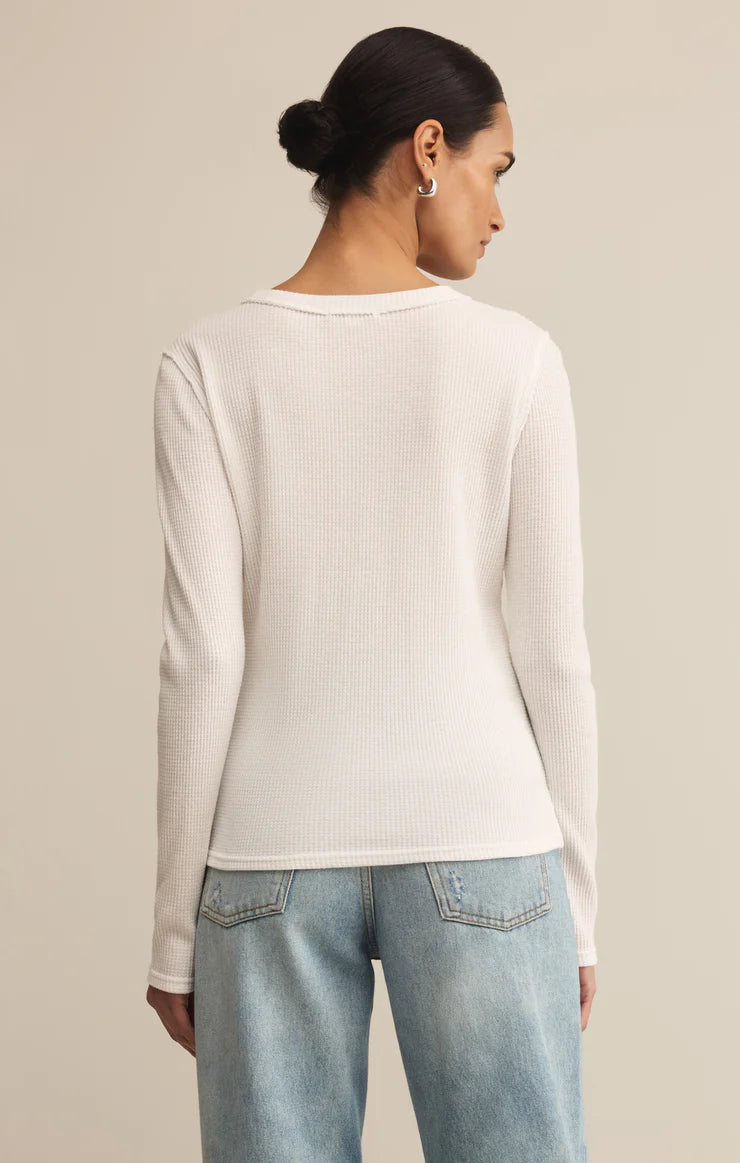 Person wearing a white ribbed sweater and light blue jeans against a beige background