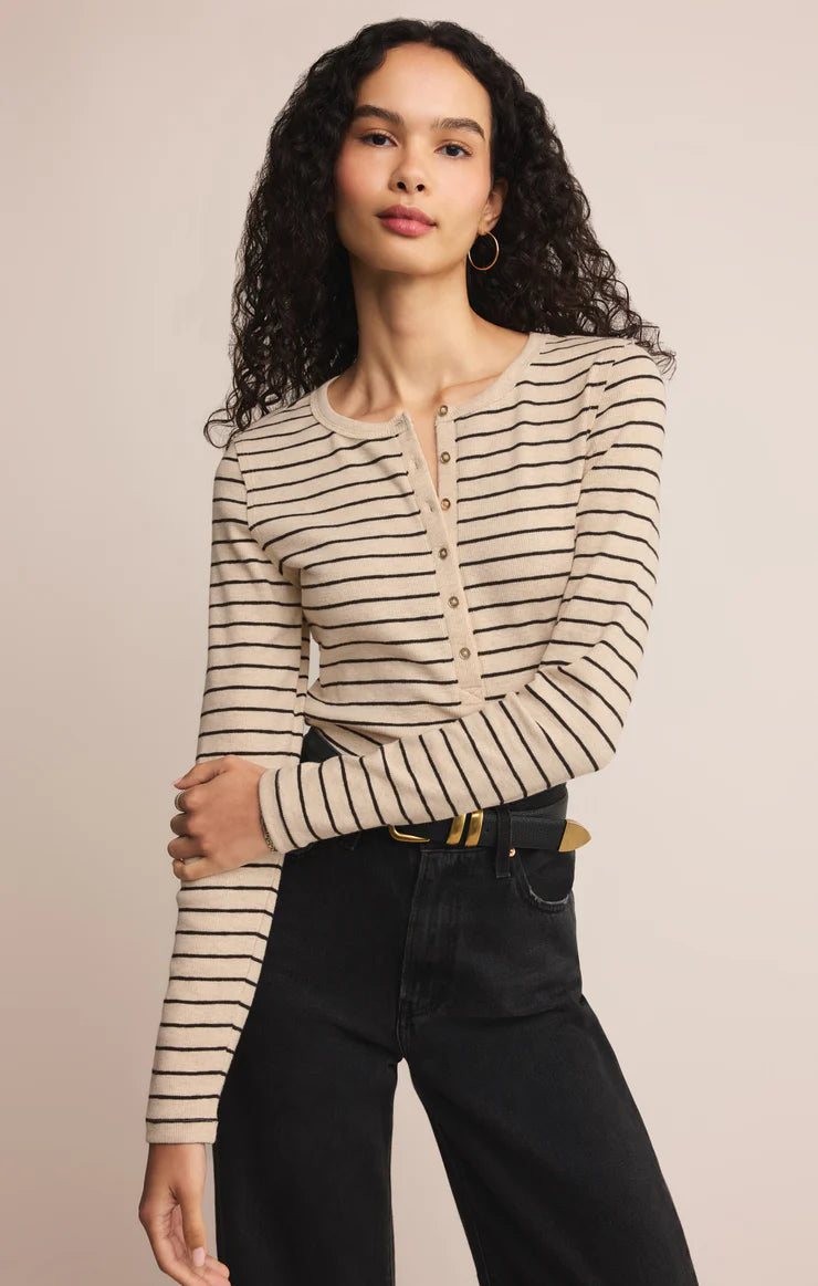 Woman wearing a striped long-sleeve top and black pants against a beige background