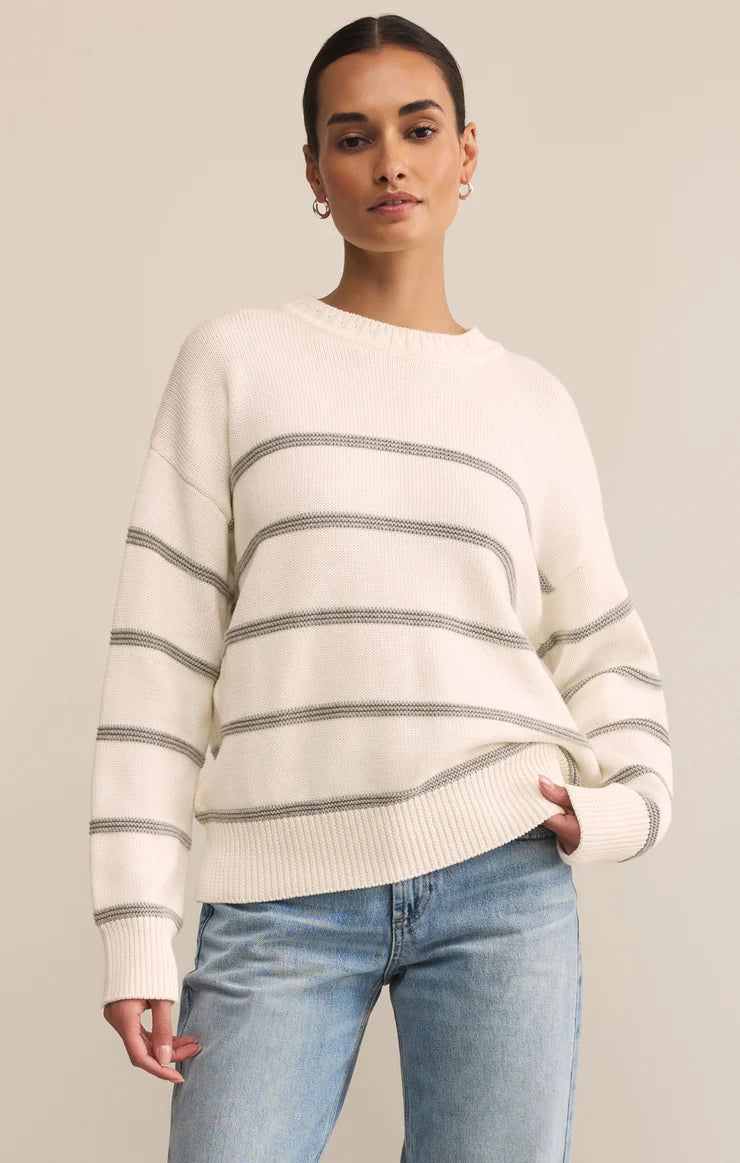 Woman wearing a white sweater with gray stripes and blue jeans on a beige background