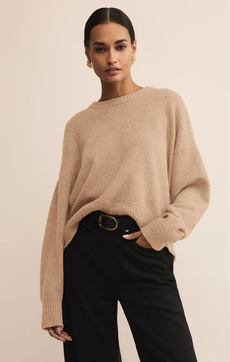 Woman wearing a beige sweater and black pants against a beige background