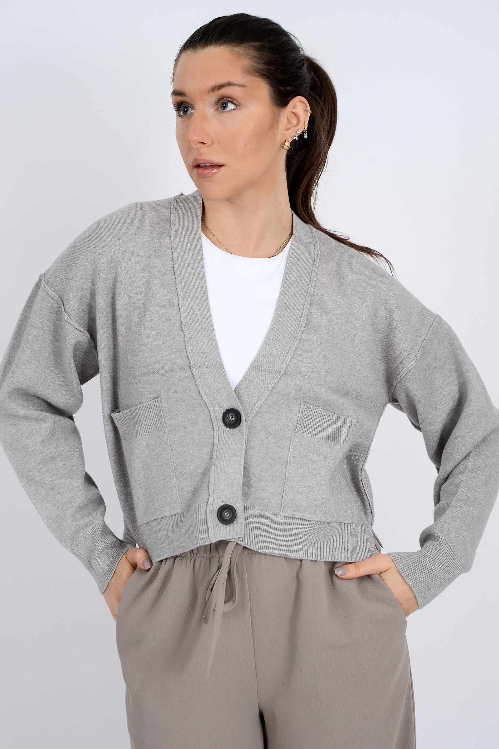 Woman wearing a gray cardigan over a white shirt with beige pants on a light gray background