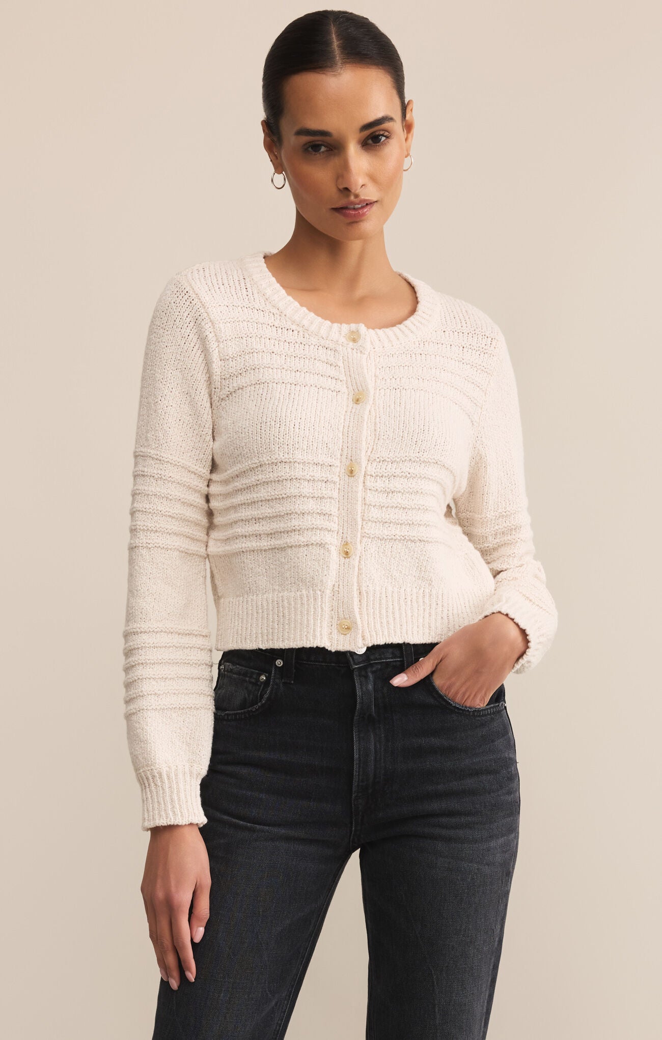 Woman wearing a cream cardigan and dark jeans against a beige background