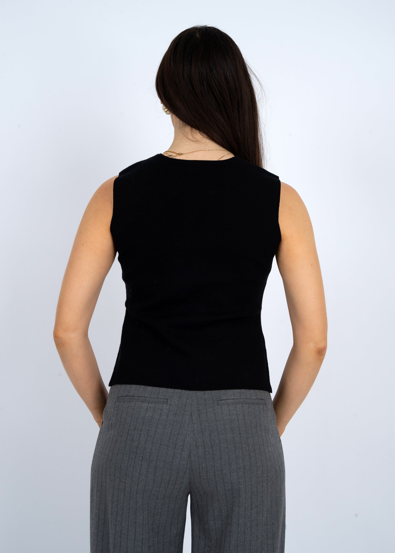 Person wearing a black sleeveless top and gray pants against a white background
