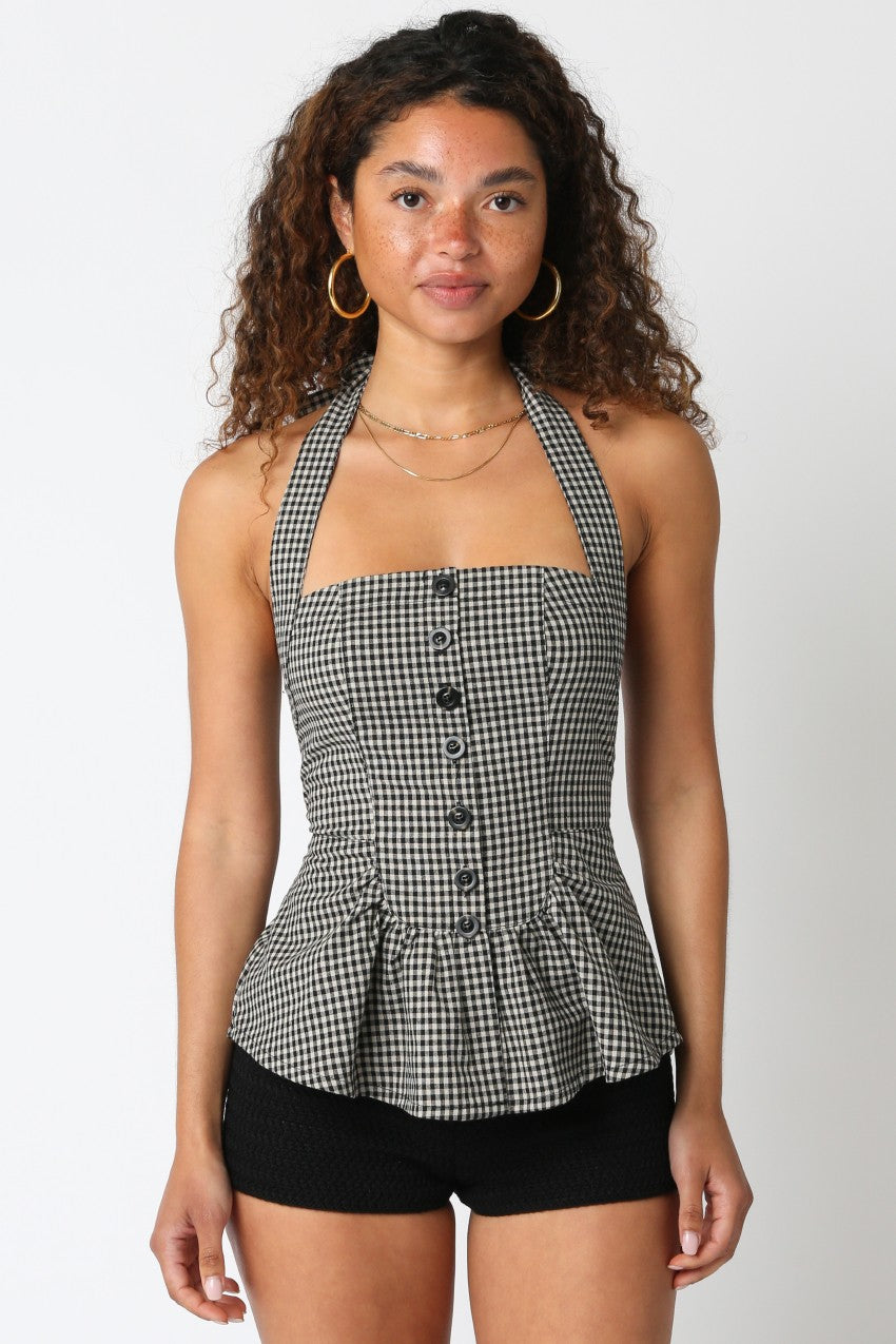 Woman wearing a black and white checkered halter top with buttons on a plain background