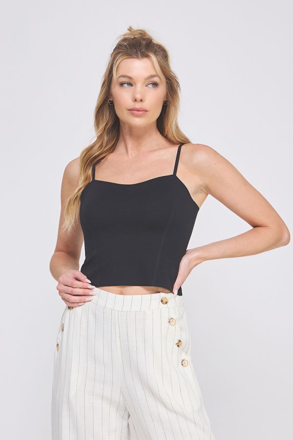 Woman wearing a black top and white pants with gold buttons on a plain background