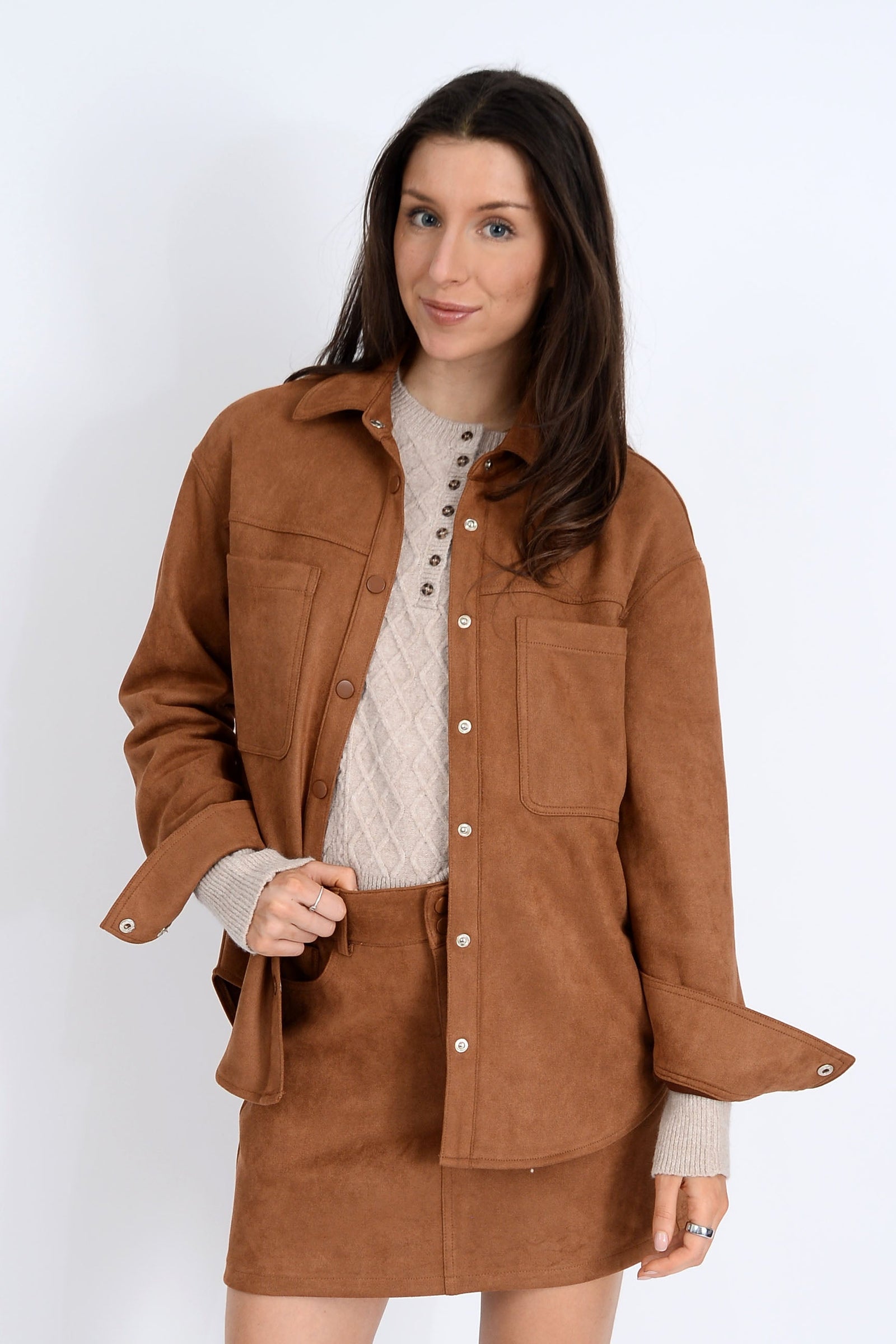 Woman wearing a brown jacket over a white sweater on a white background