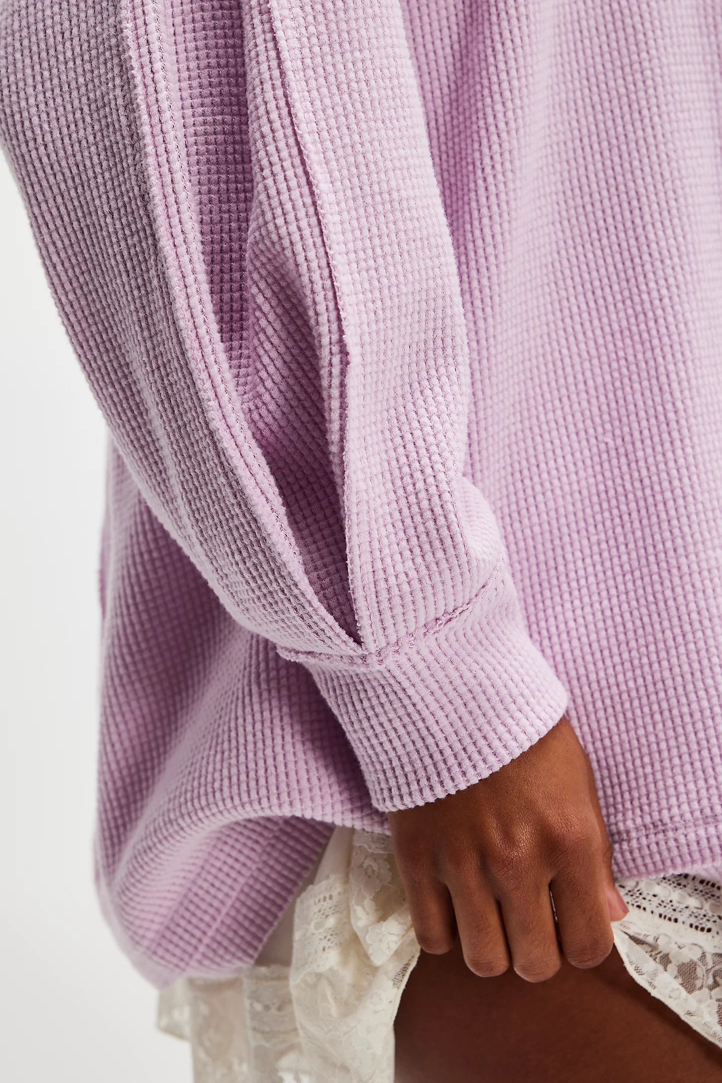 Close-up of a person wearing a textured purple long-sleeve top with a neutral background