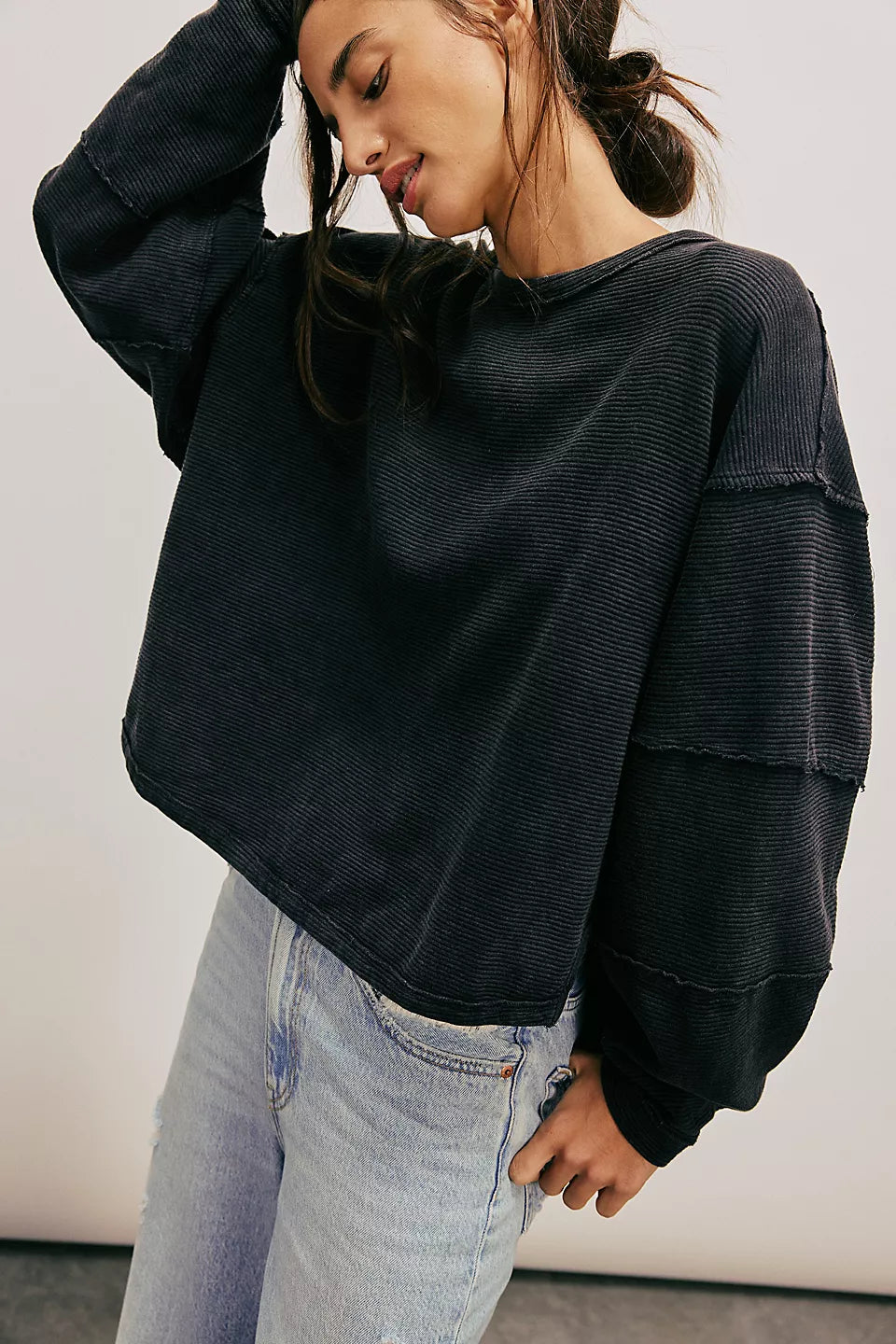 Woman wearing a black oversized sweater and light blue jeans against a plain background