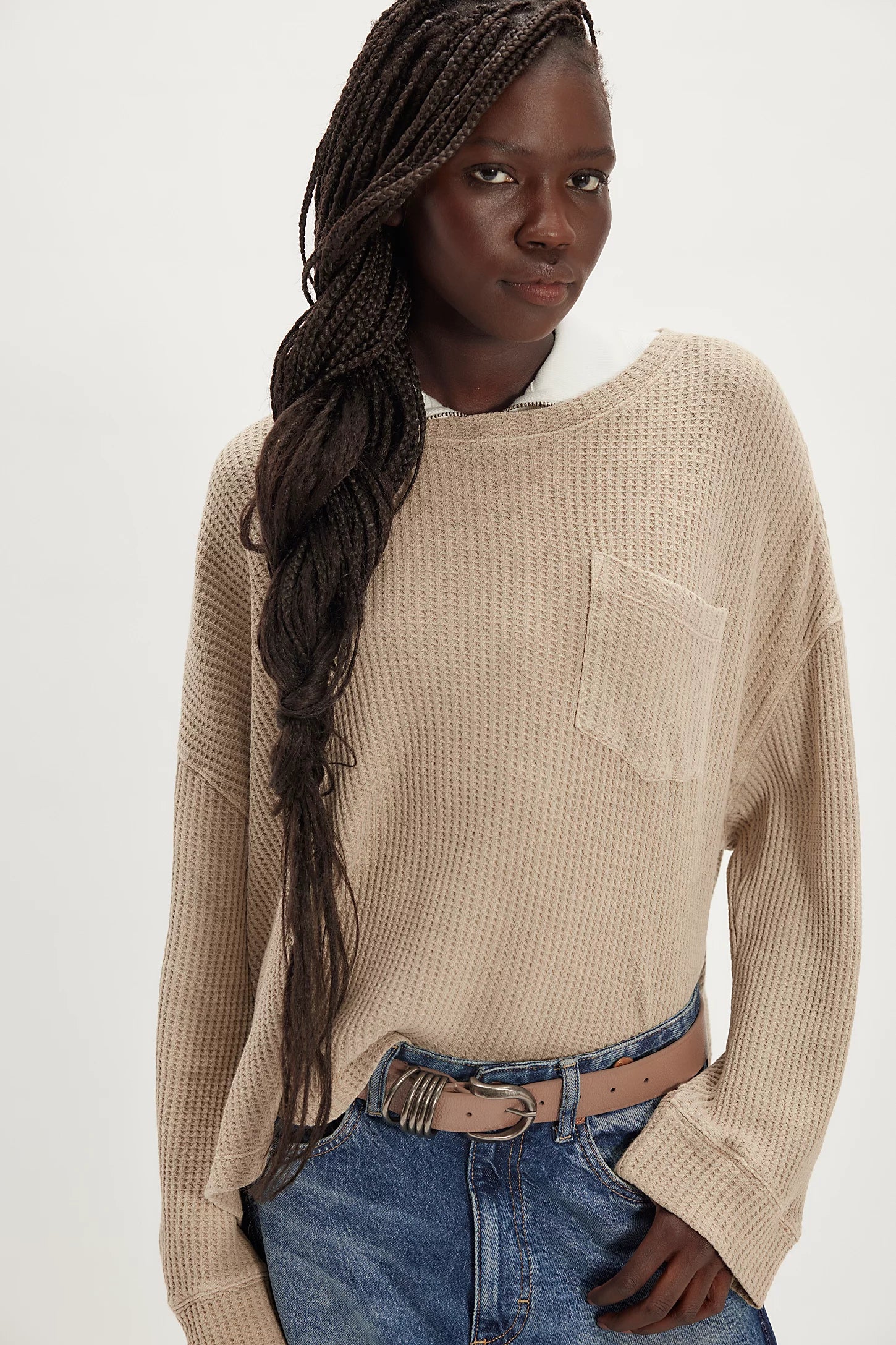 Woman wearing a beige sweater and blue jeans on a white background