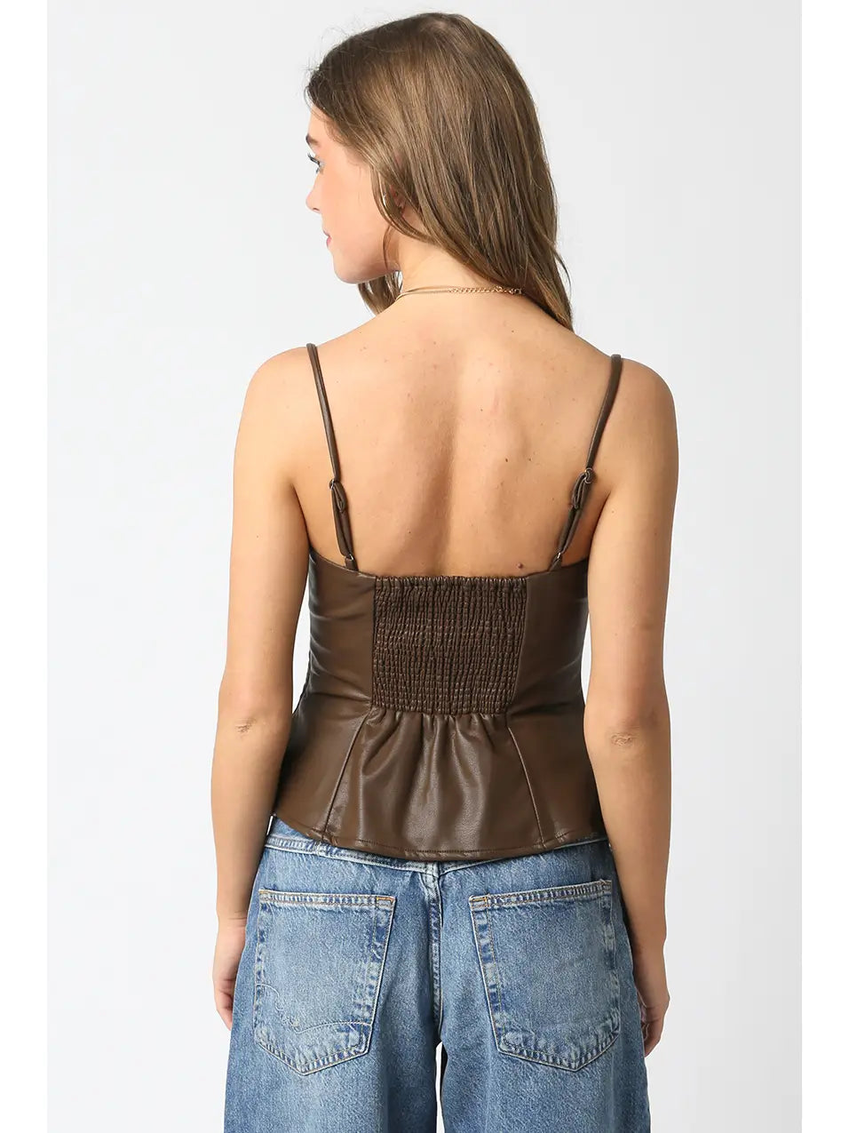 Woman wearing a brown leather top and blue jeans on a white background