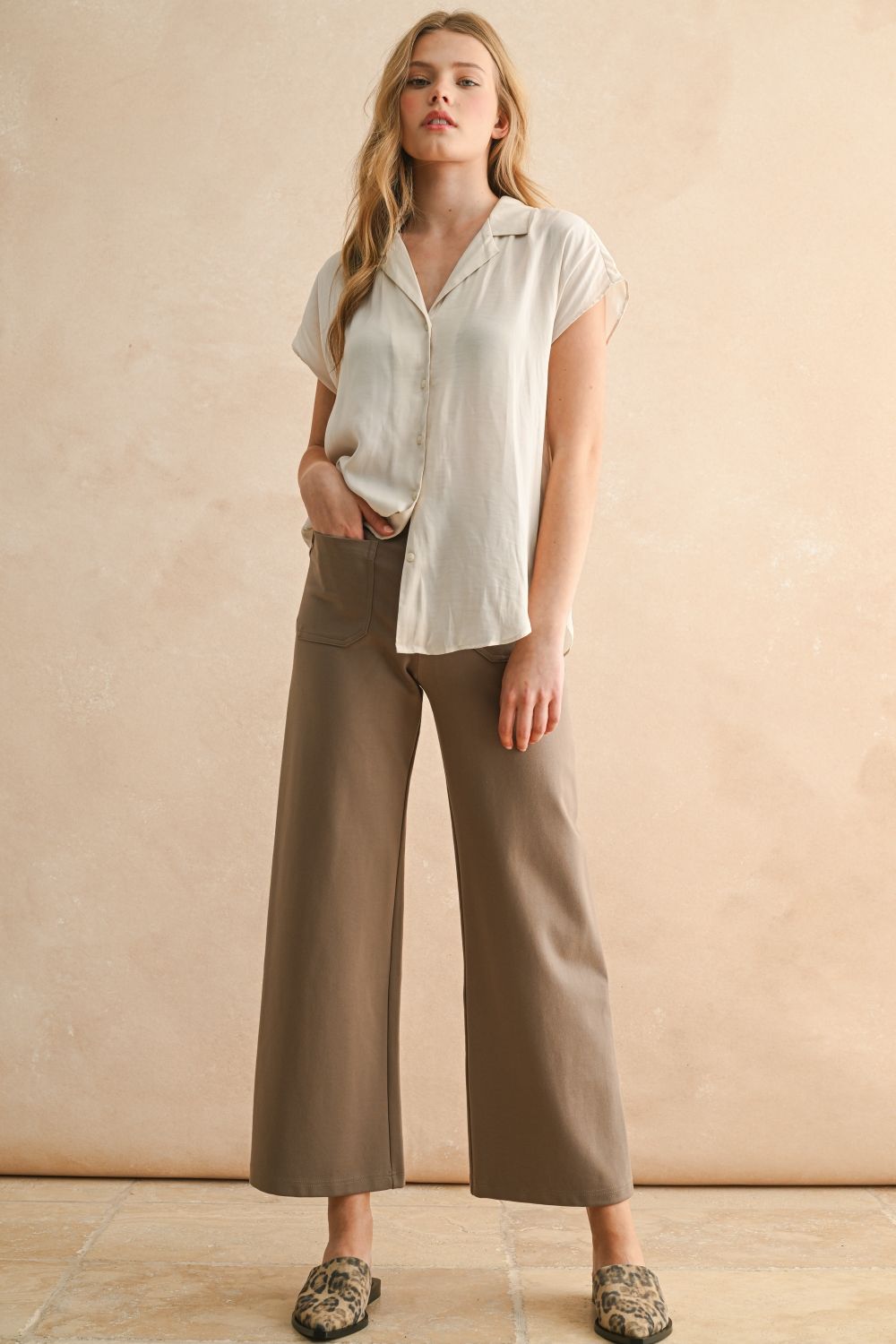 Woman wearing a white blouse and brown pants against a beige background
