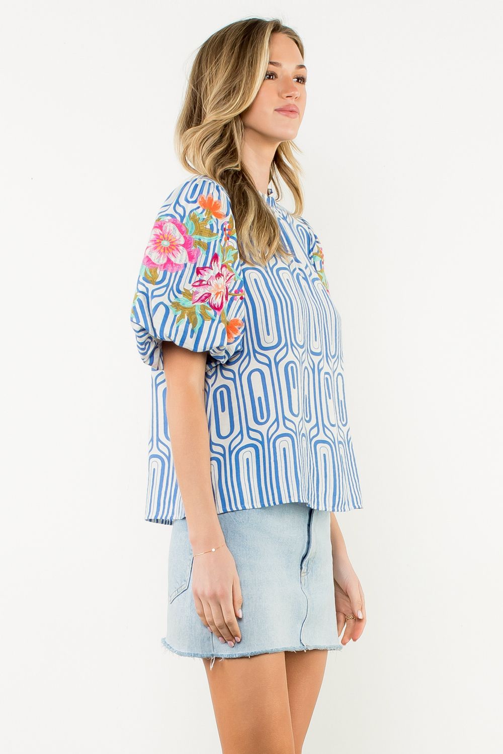 Woman wearing a blue patterned blouse with floral sleeves on a white background