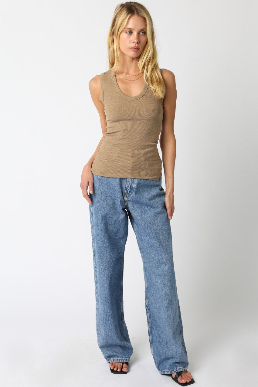 Woman wearing a beige tank top and blue jeans on a white background