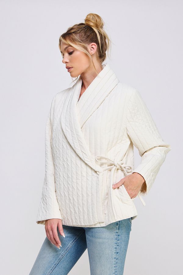 Woman wearing a cream-colored cable knit cardigan over a white top with light blue jeans on a plain background