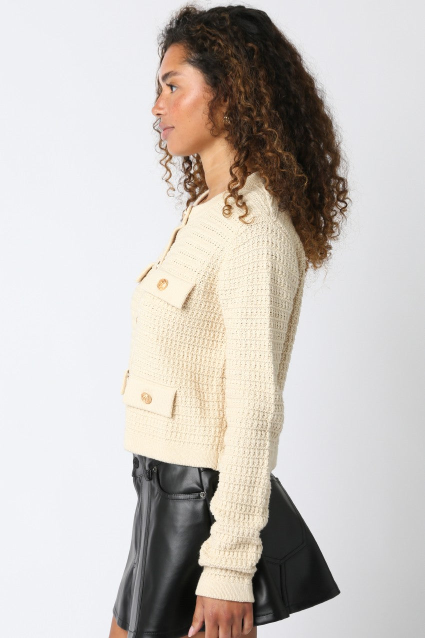 Woman wearing a cream-colored textured jacket and black leather skirt on a white background