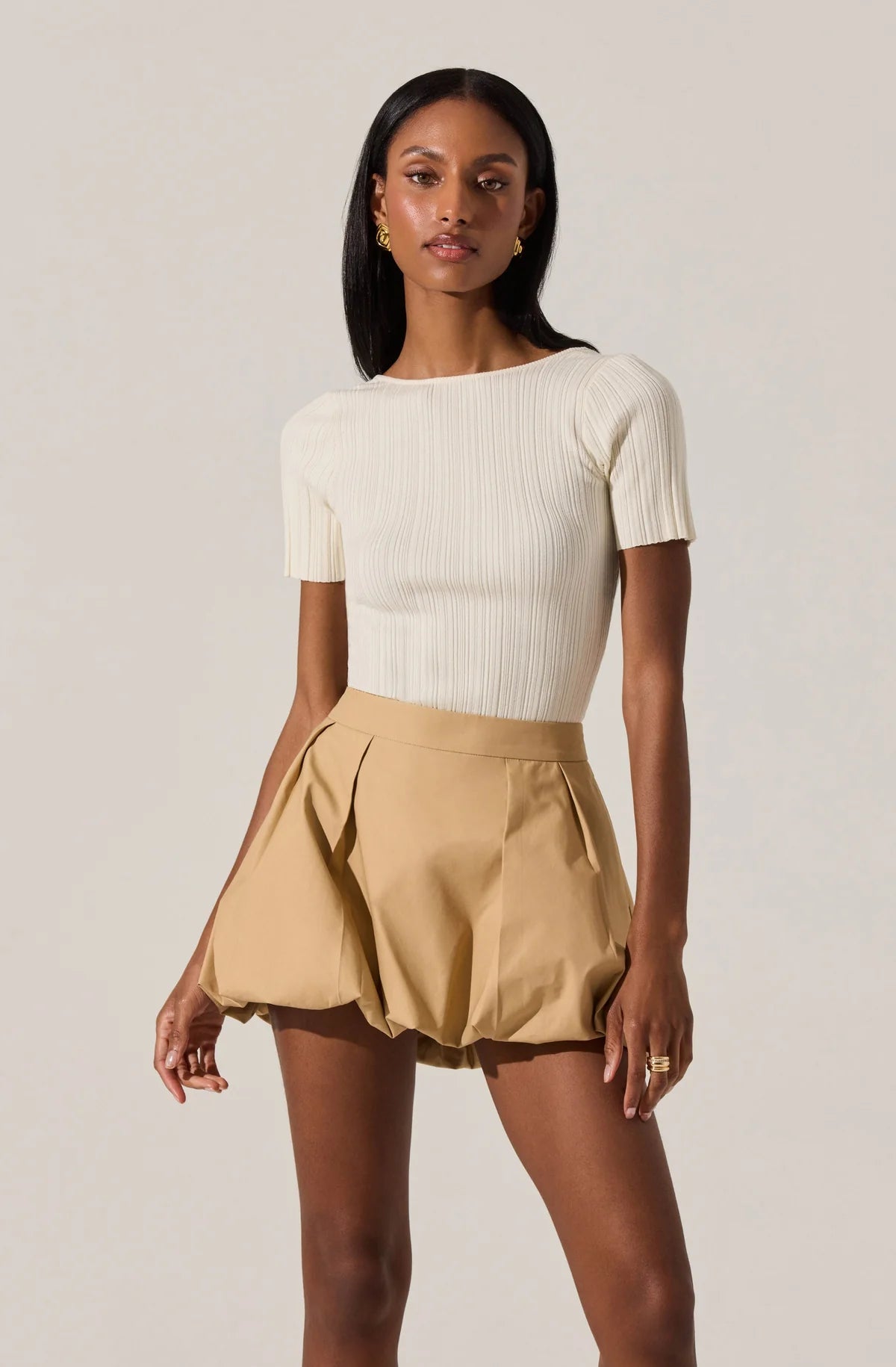 Woman wearing a white ribbed top and beige skirt on a plain background